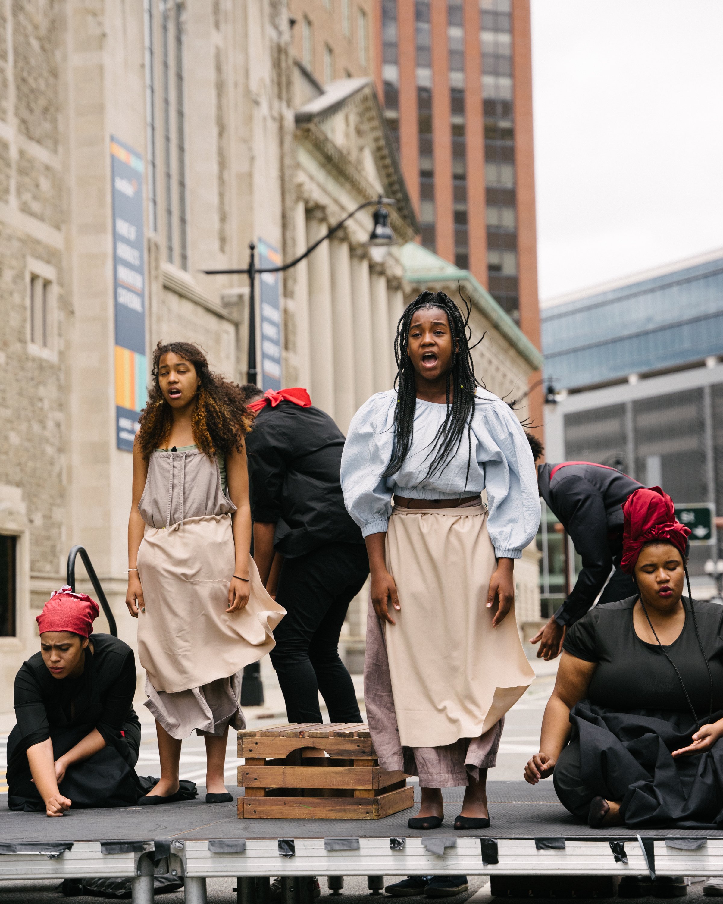 Photo By Bryon Summers
Jada Clark and Kazoani Gonmiah stand singing forward, as other Aurway Artists portray slaves around them. Behind them is the historic Newark Main Library.