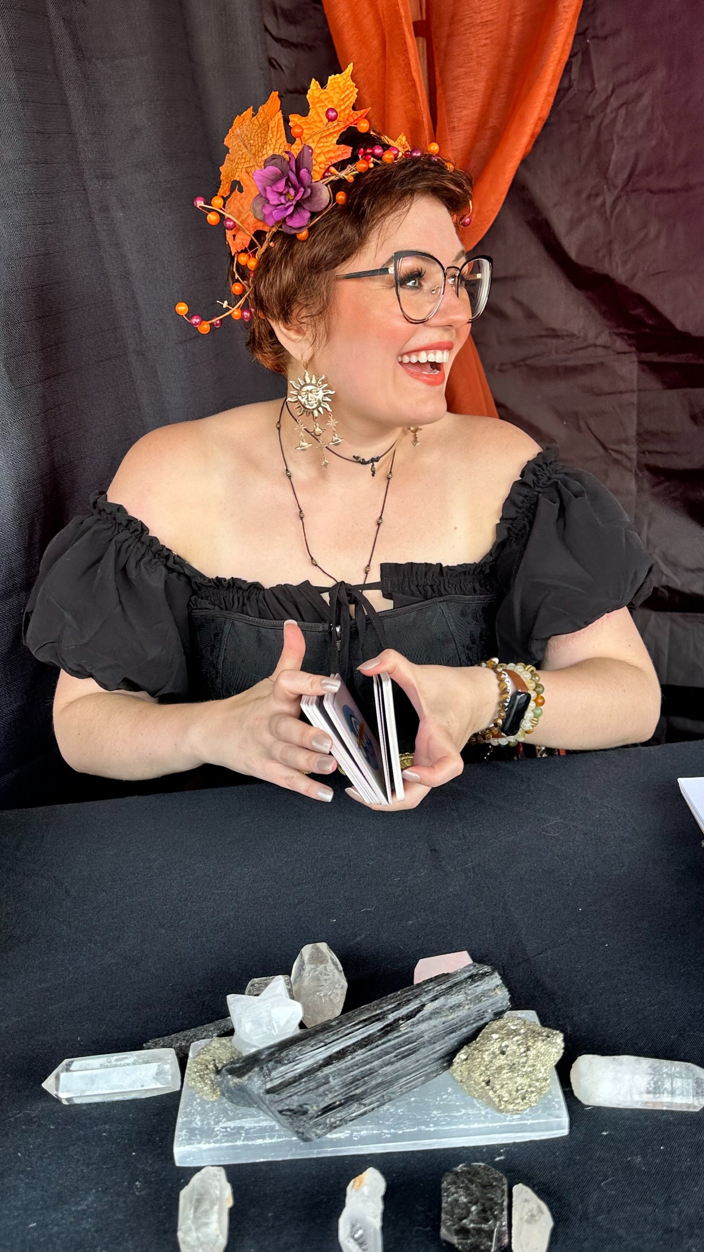 Madame Creatrix smiles off camera while shuffling cards in her tent at a festival.