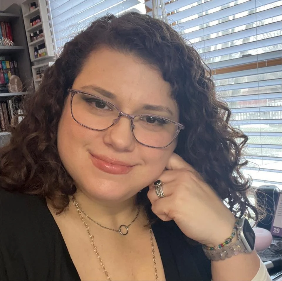 Hands holding a crystal ball on a wooden table with incense and a book nearby.