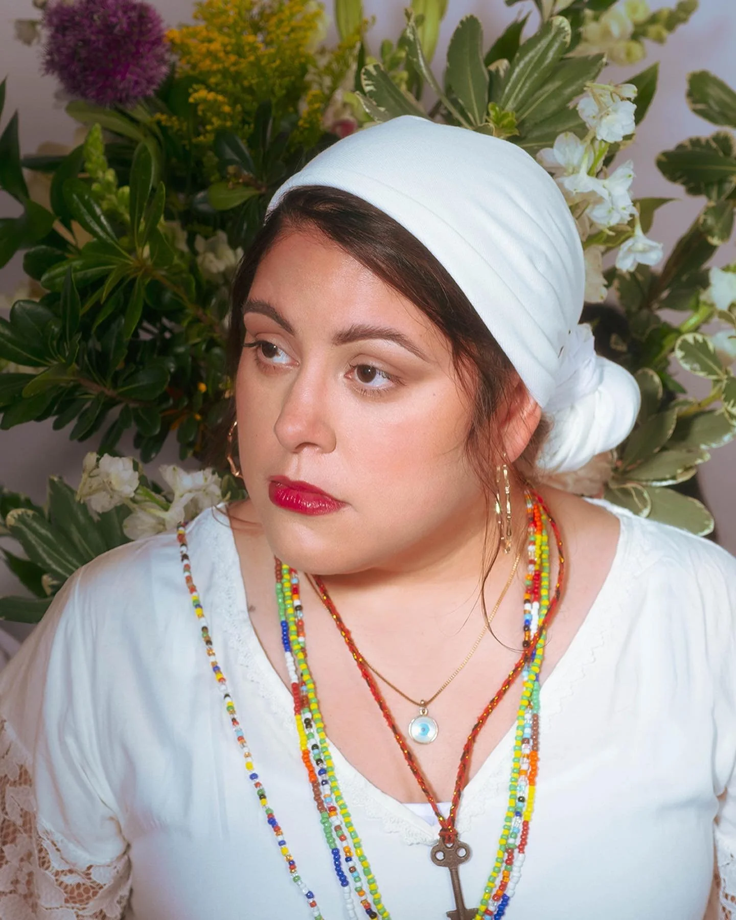 Beautiful bruja veiled in white, with many beaded necklaces and dangling earrings.