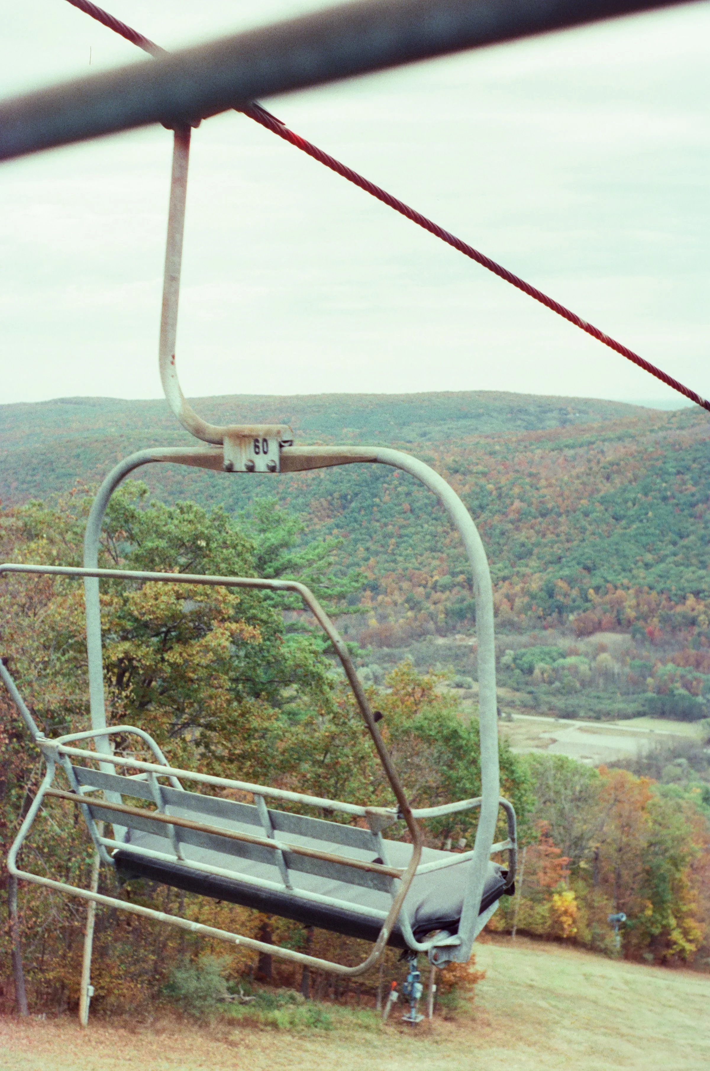 An empty ski lift chair hanging in midair with a view of colorful autumn trees and hills.