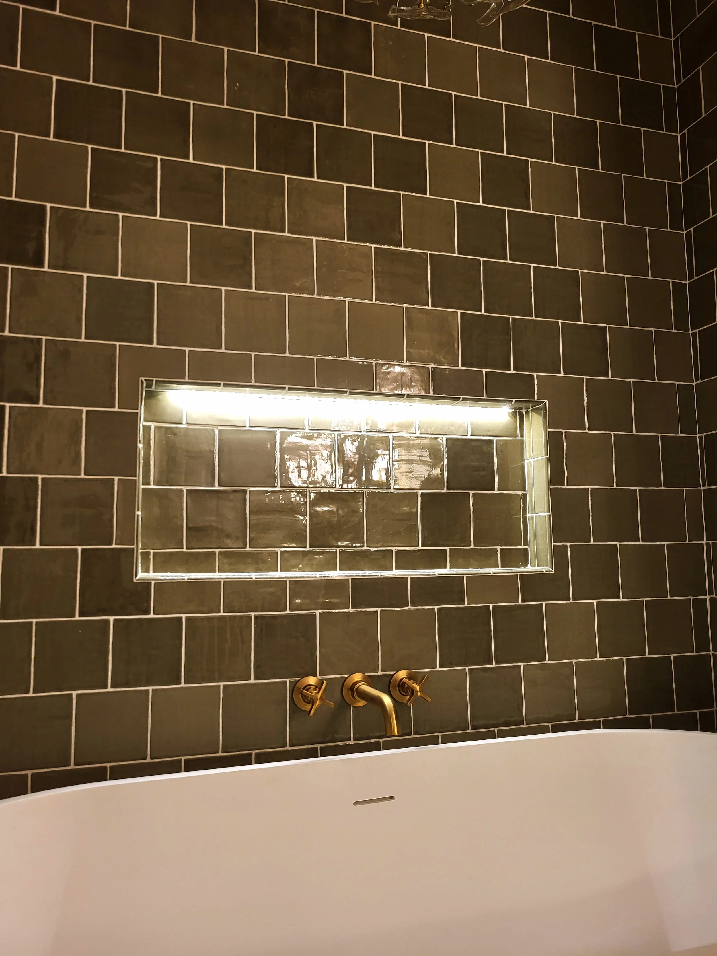 Illuminated niche above a wall mounted tub faucet.