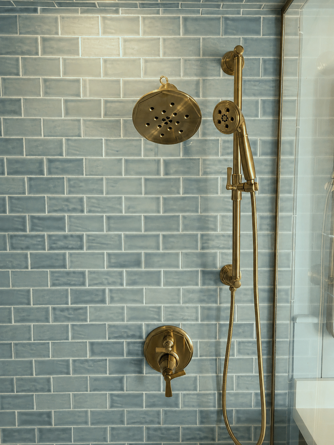 A modern brass shower head and faucet, with an adjustable handheld shower attachment.