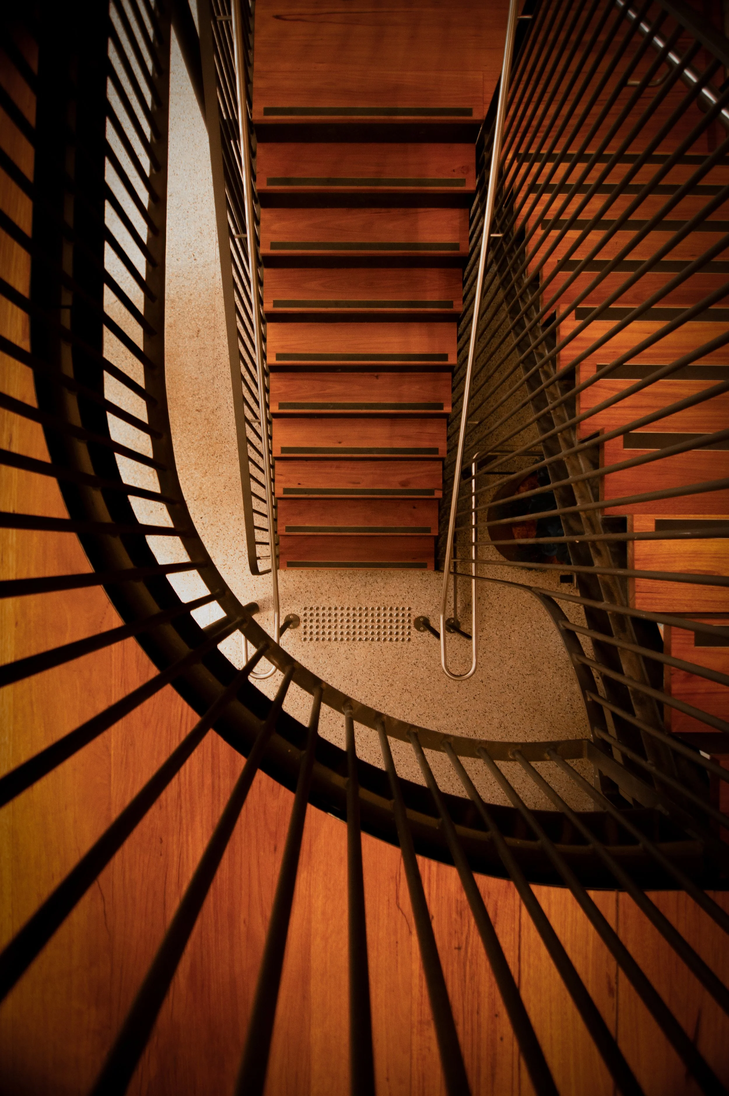Overhead view of a spiral staircase at Handle Branding Agency with wooden steps and black metal railings on a wooden floor.