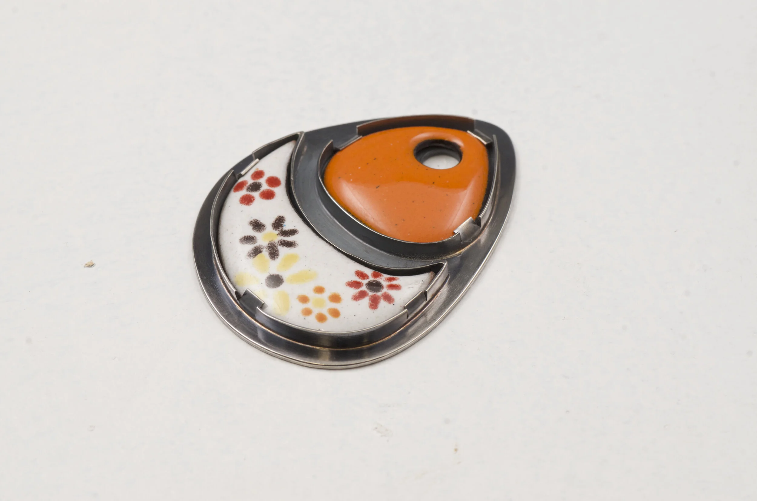 A decorative button with floral pattern and an orange gemstone in a black metal setting.