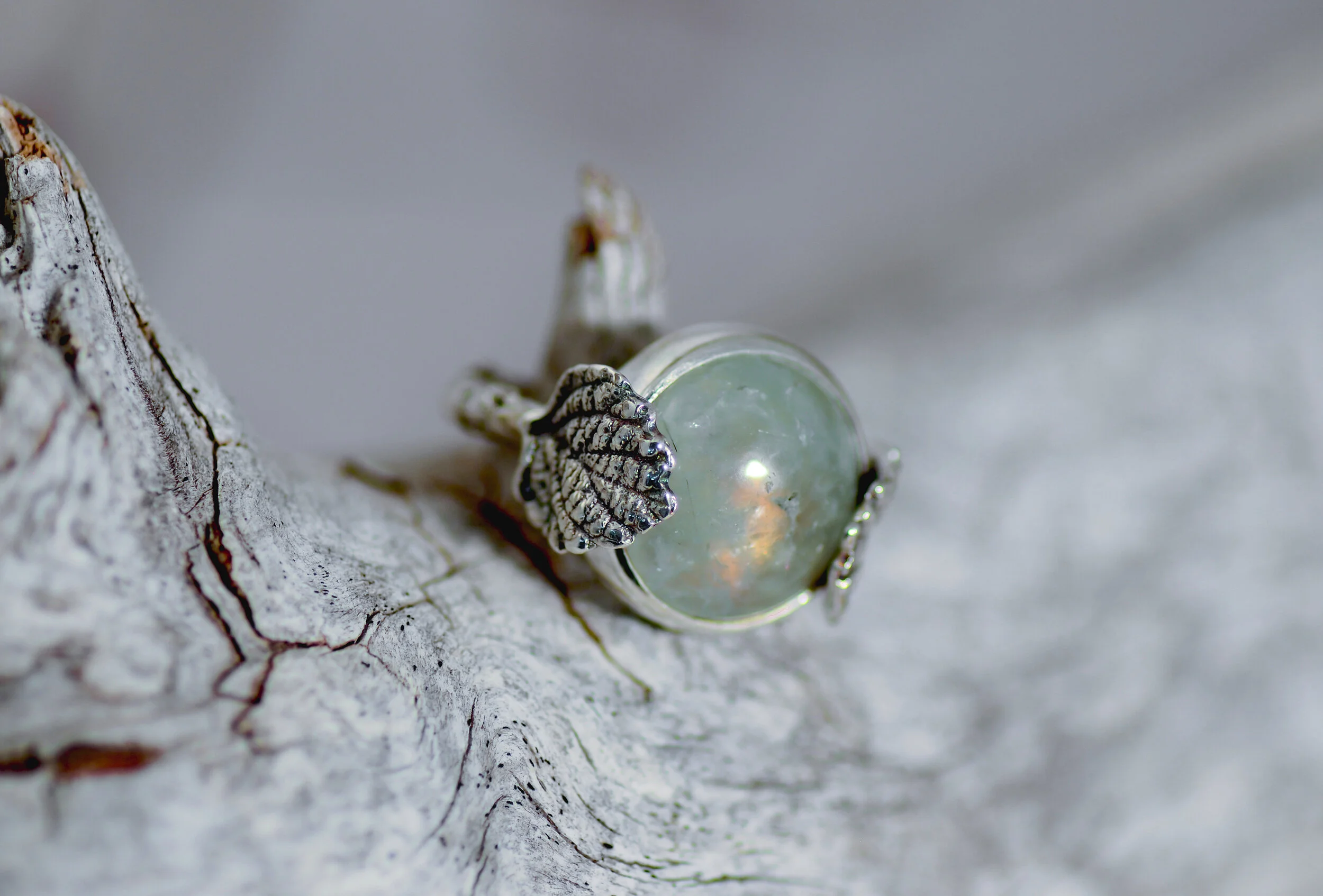 A piece of jewelry with a spherical, iridescent stone and metallic decorative elements, resting on a textured, cracked surface.