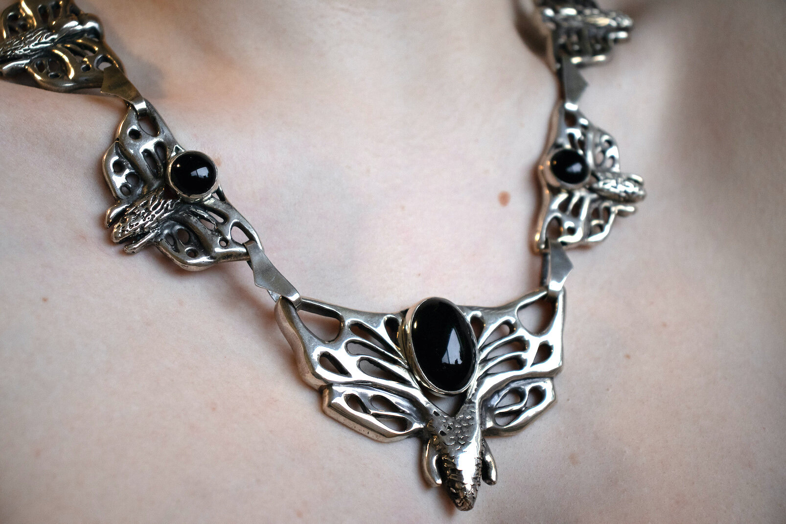 A silver necklace with butterfly-shaped designs and black oval stones worn around a person's neck.