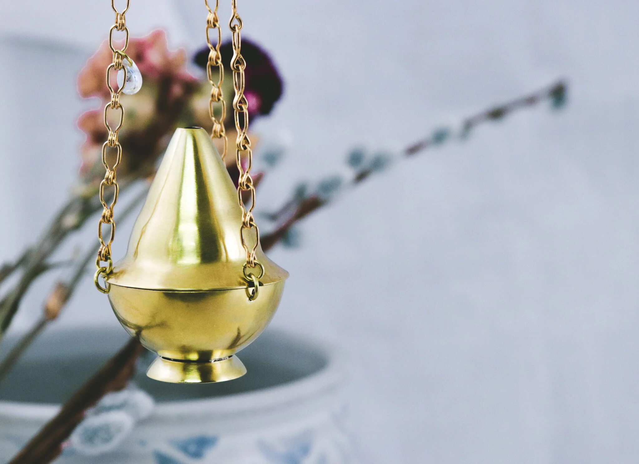 A golden spinning top toy hanging from a chain, with a blurred background of pink flowers and a plant branch.