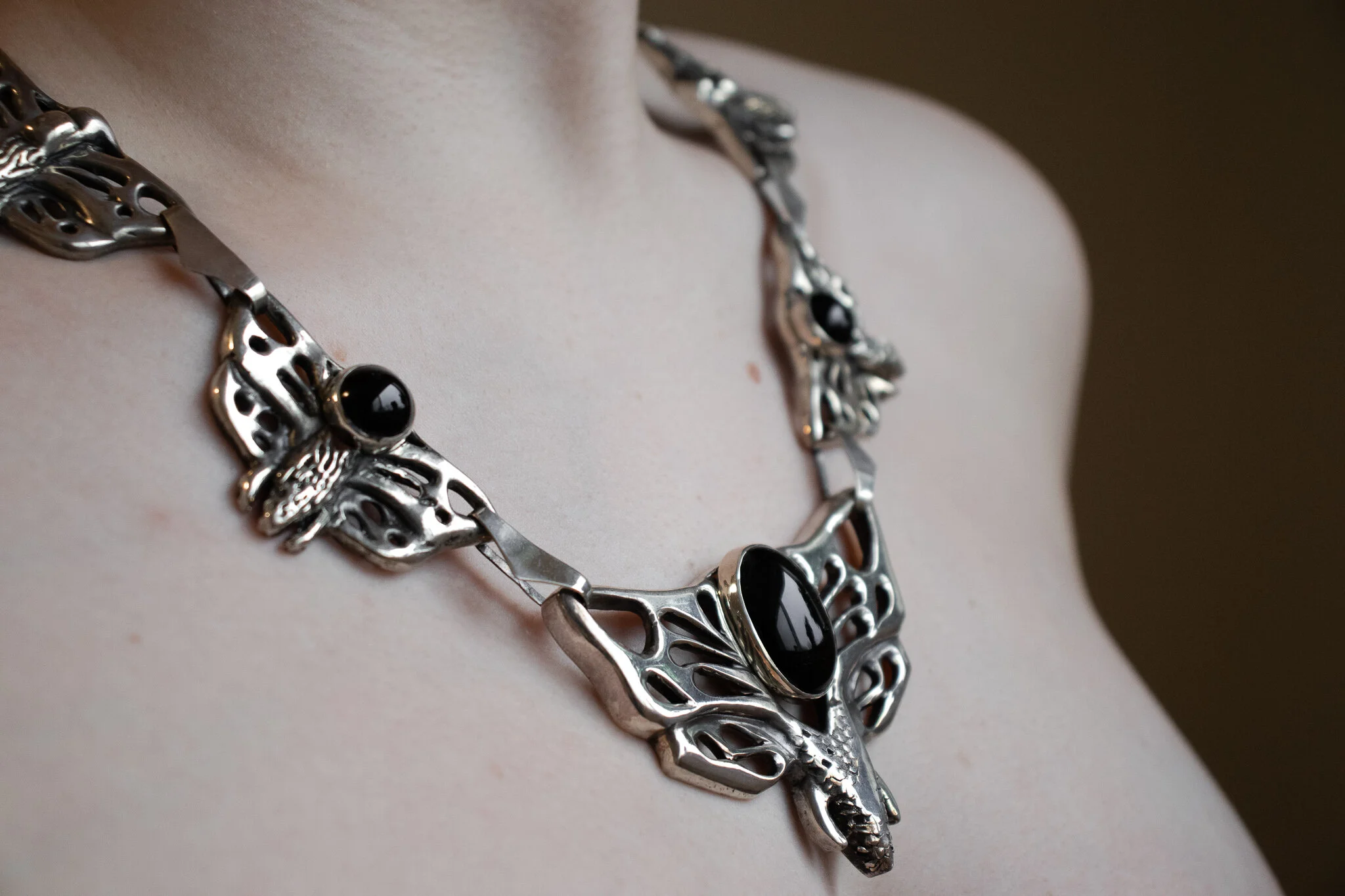 Close-up of a silver butterfly-shaped necklace with black stones worn on a person's neck and chest.