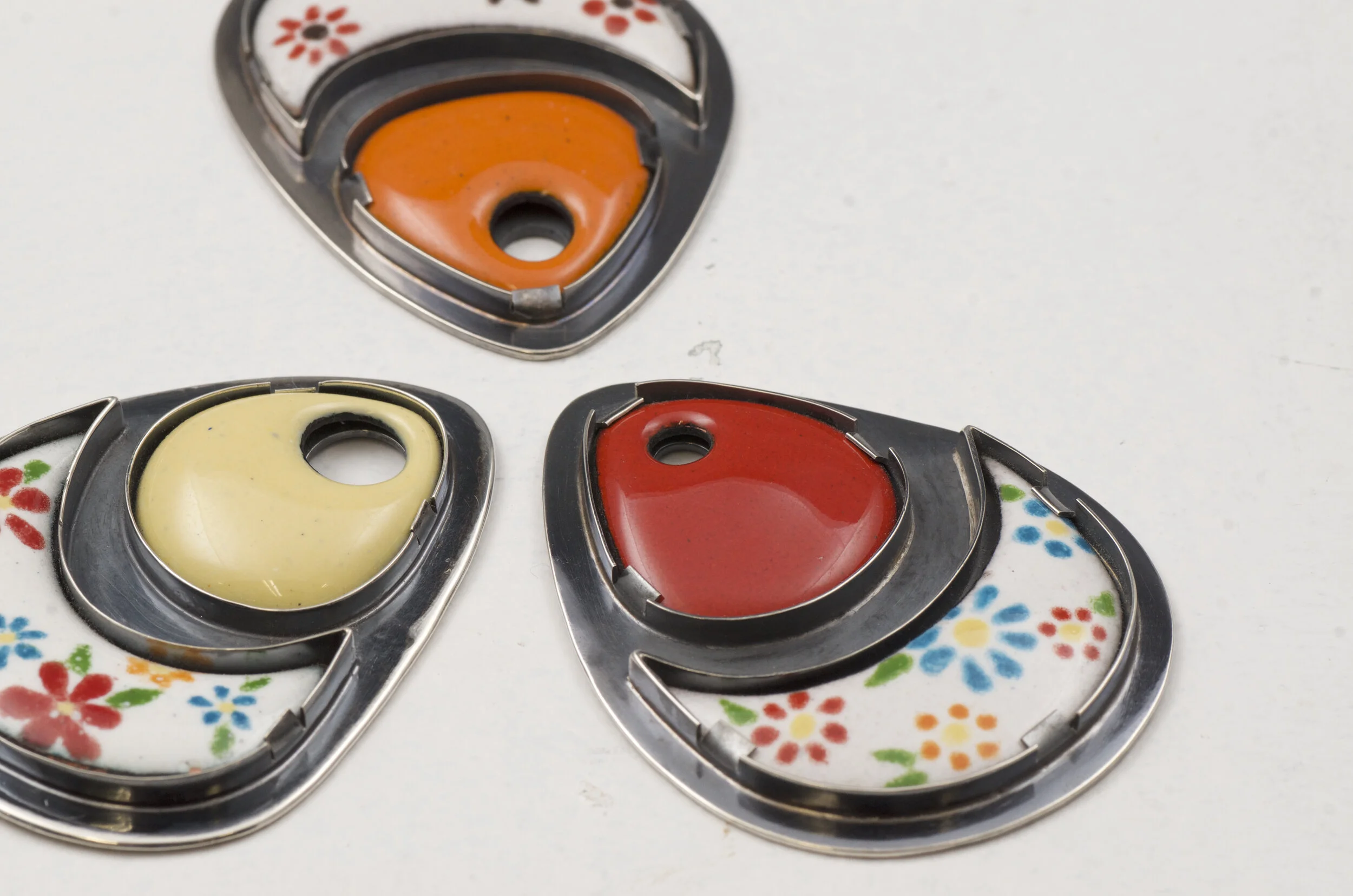 Three vintage heart-shaped tins with colorful floral designs, each containing a different colored substance: orange, yellow, and red, on a white surface.