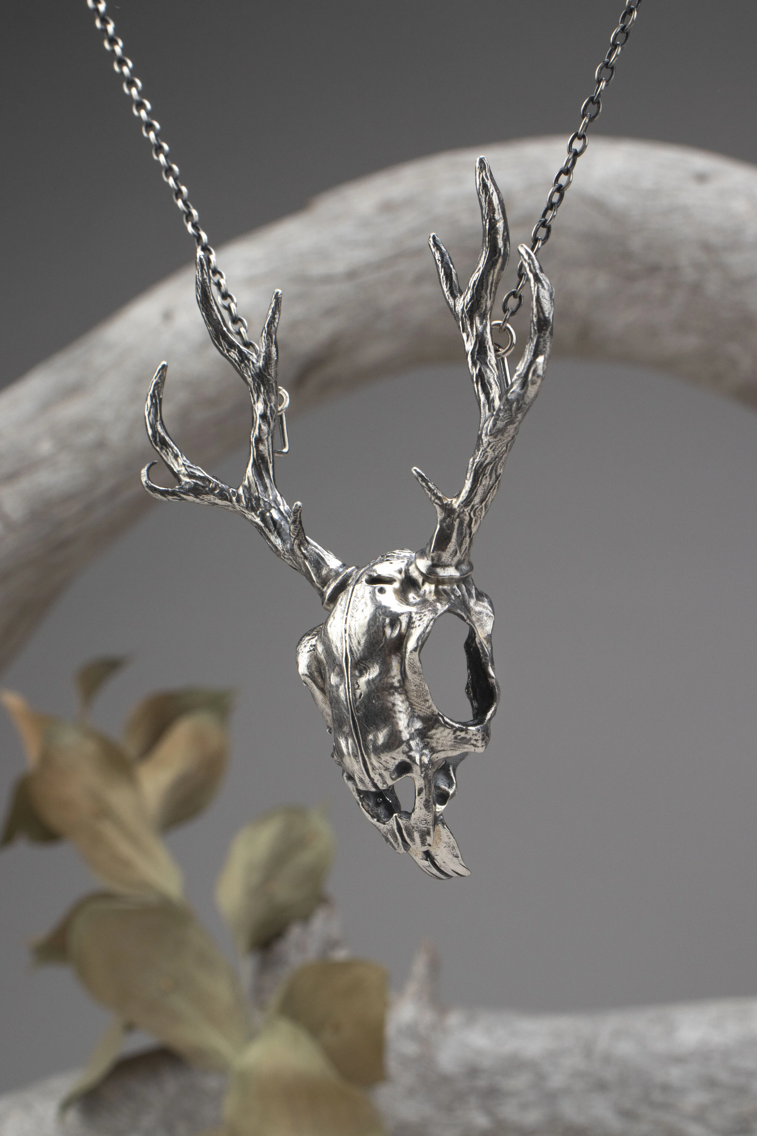 Silver pendant necklace shaped like a deer skull with antlers, hanging from a chain.