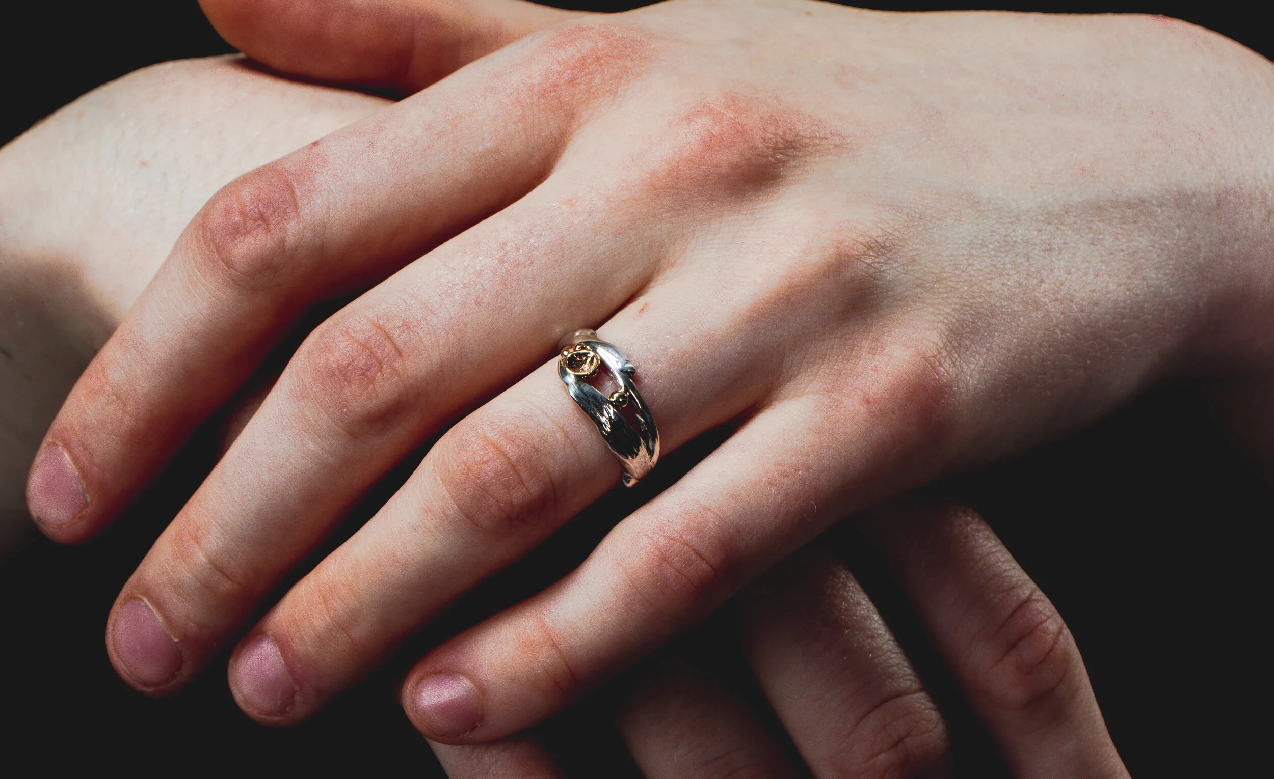 Close-up of a person's hand with a multi-tone metal ring on the middle finger, against a black background.