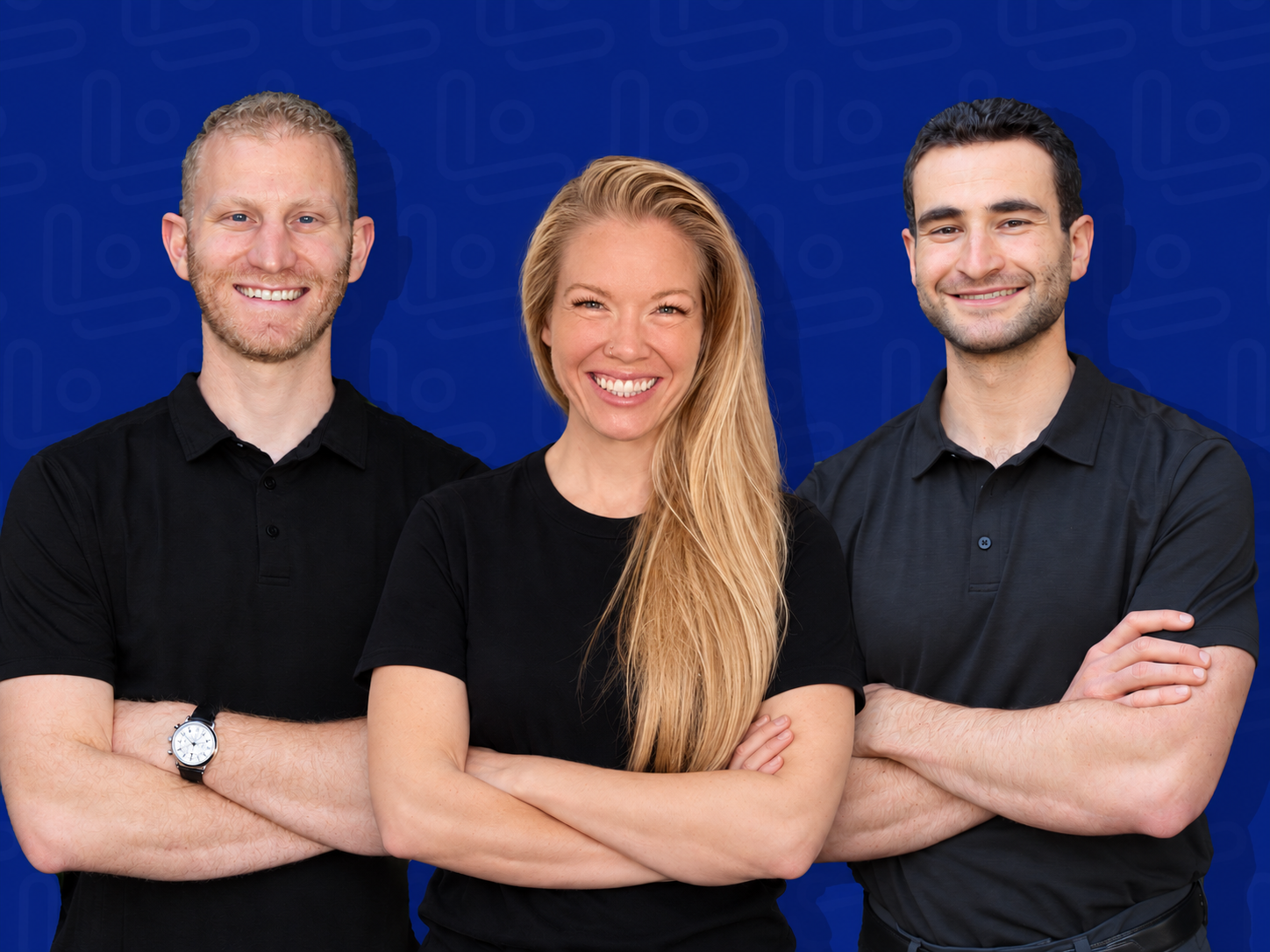 Three happy young adults with arms crossed smiling against a blue background.