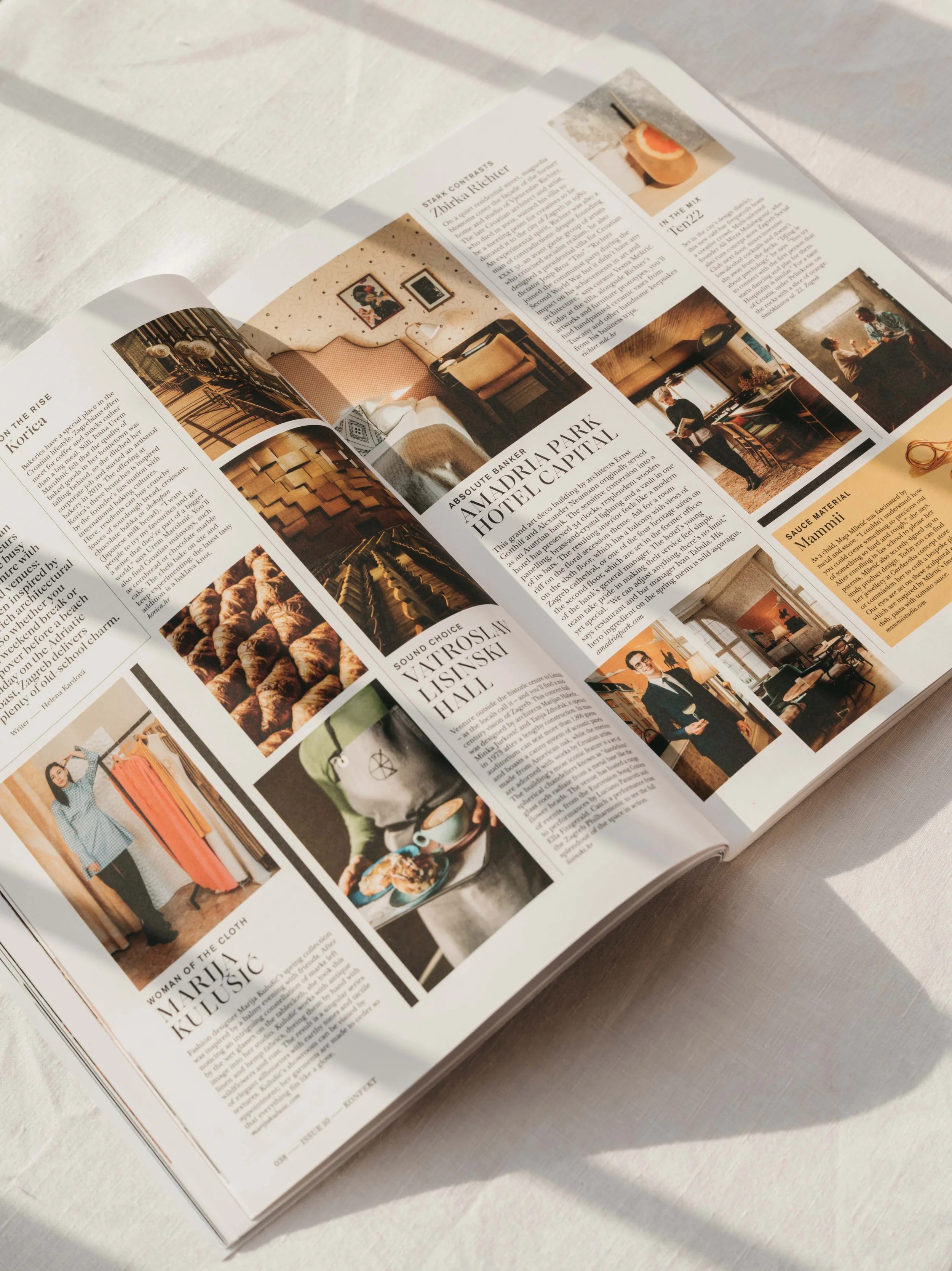 Open magazine pages showing interior design, food, and people, with sunlight casting shadow across the pages.
