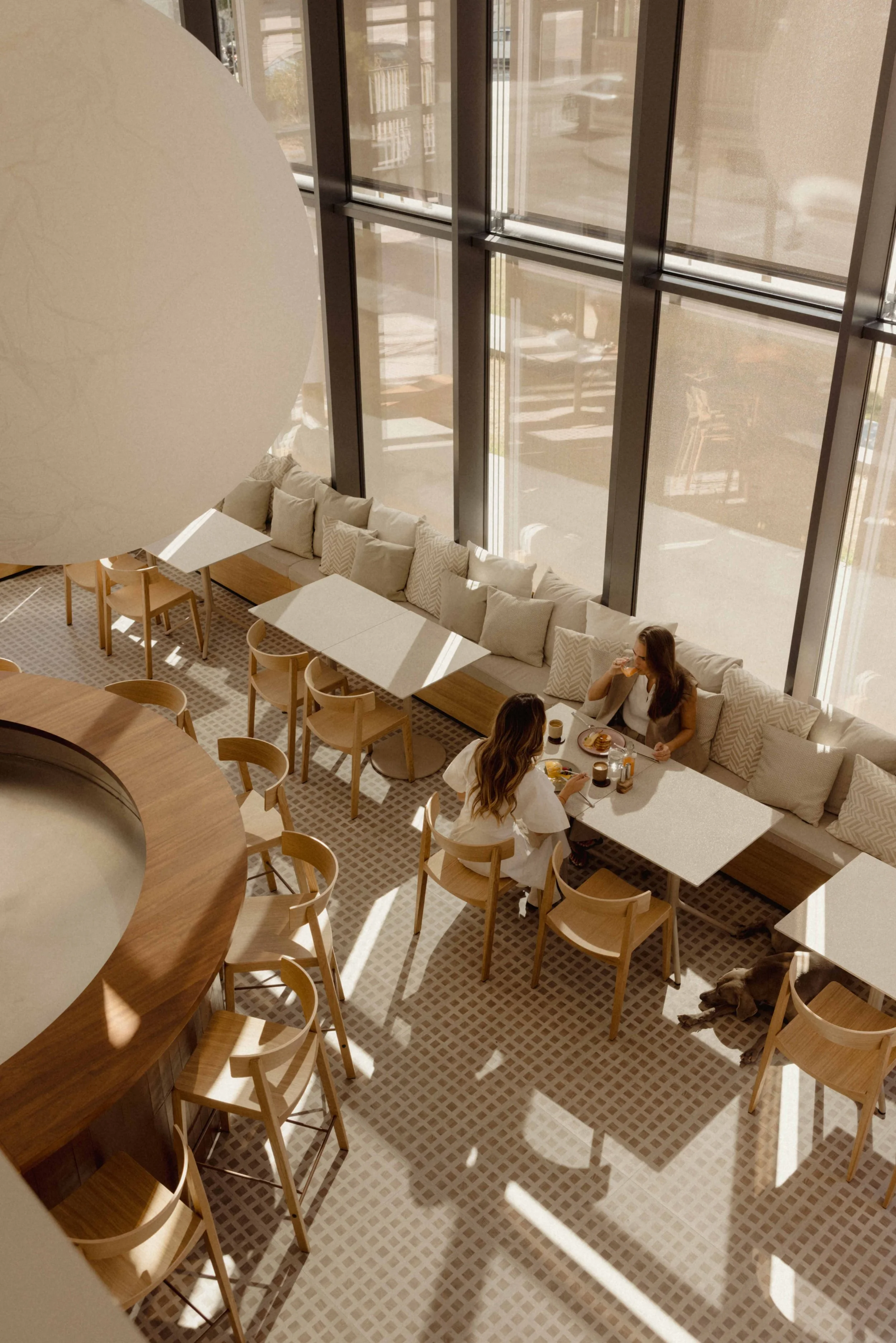 Two women having breakfast at a table in a modern cafe with large windows and natural light.