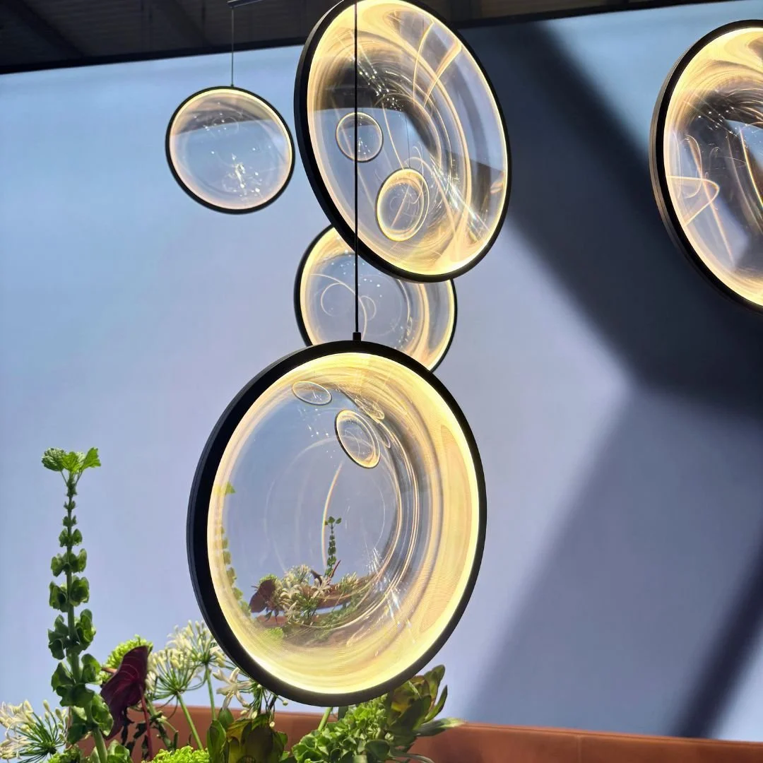 A moving light fitting from Salone del Mobile.

Designed to act as a lens, it captures and refracts light and colour from across the space &mdash; constantly shifting with its surroundings.

Part of how we source more distinctive pieces for our proje