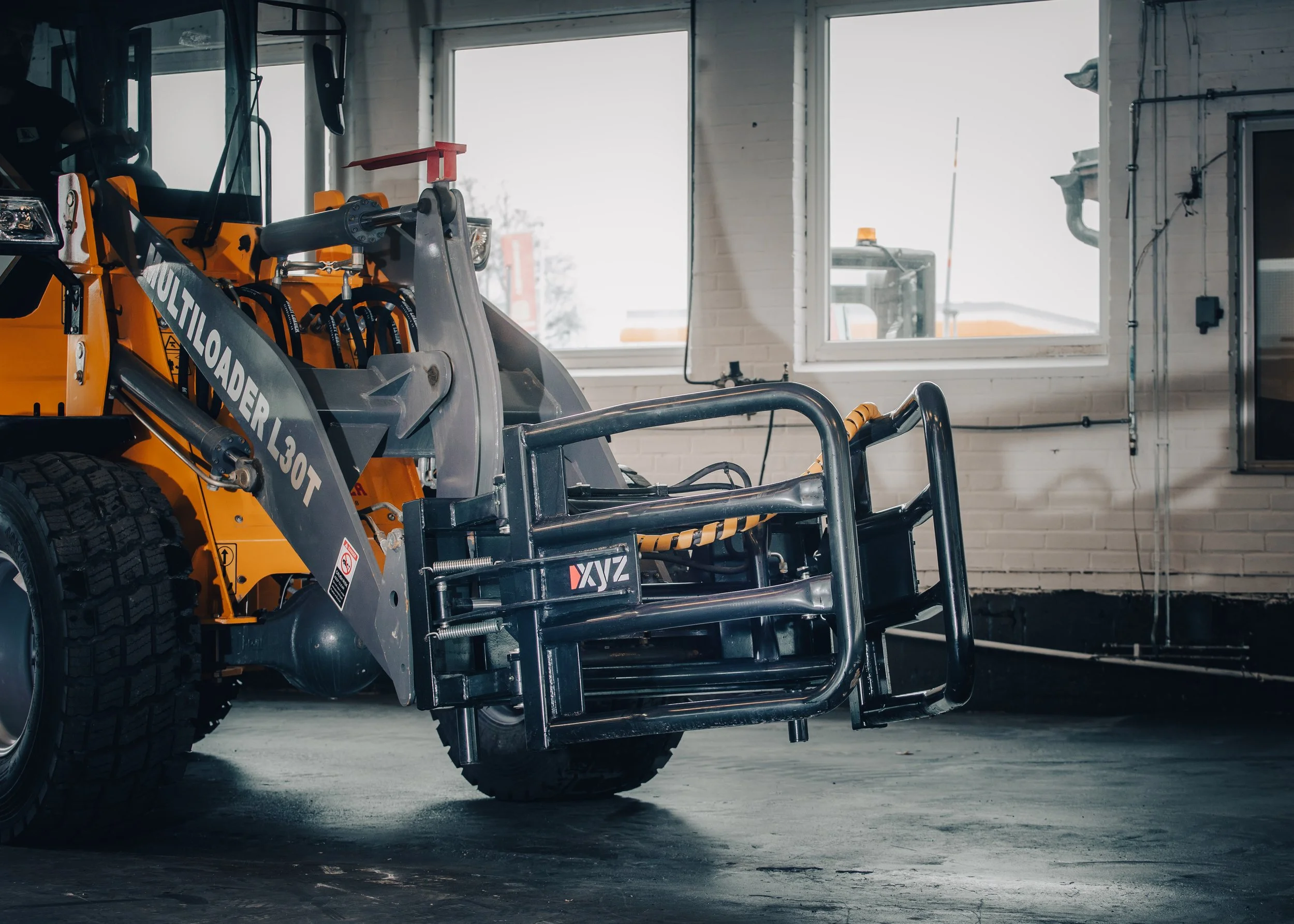 Construction or industrial vehicle with a front attachment, parked inside a building with large windows and white brick walls.