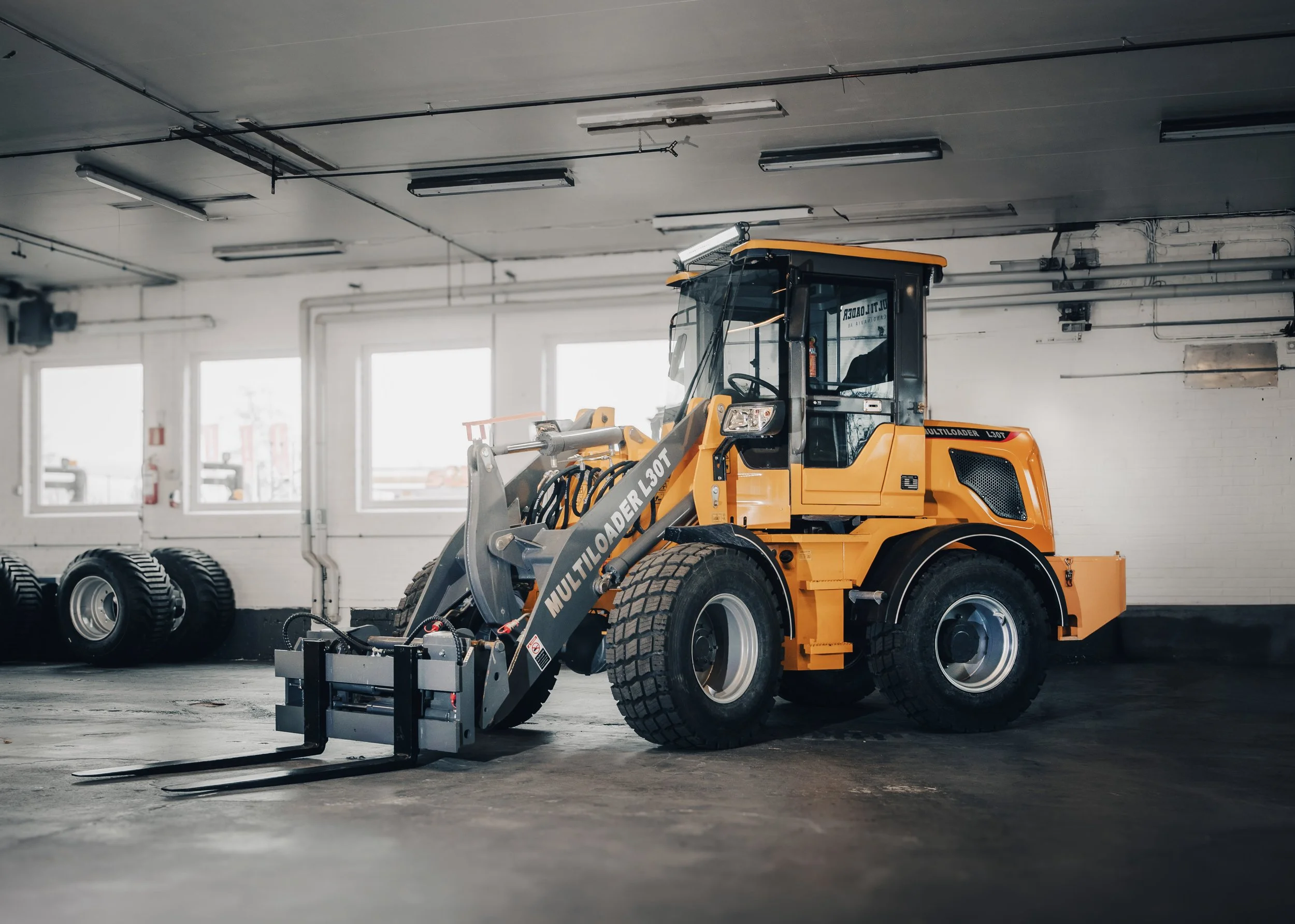 Yellow industrial loader inside a warehouse with tires stacked on the left side.