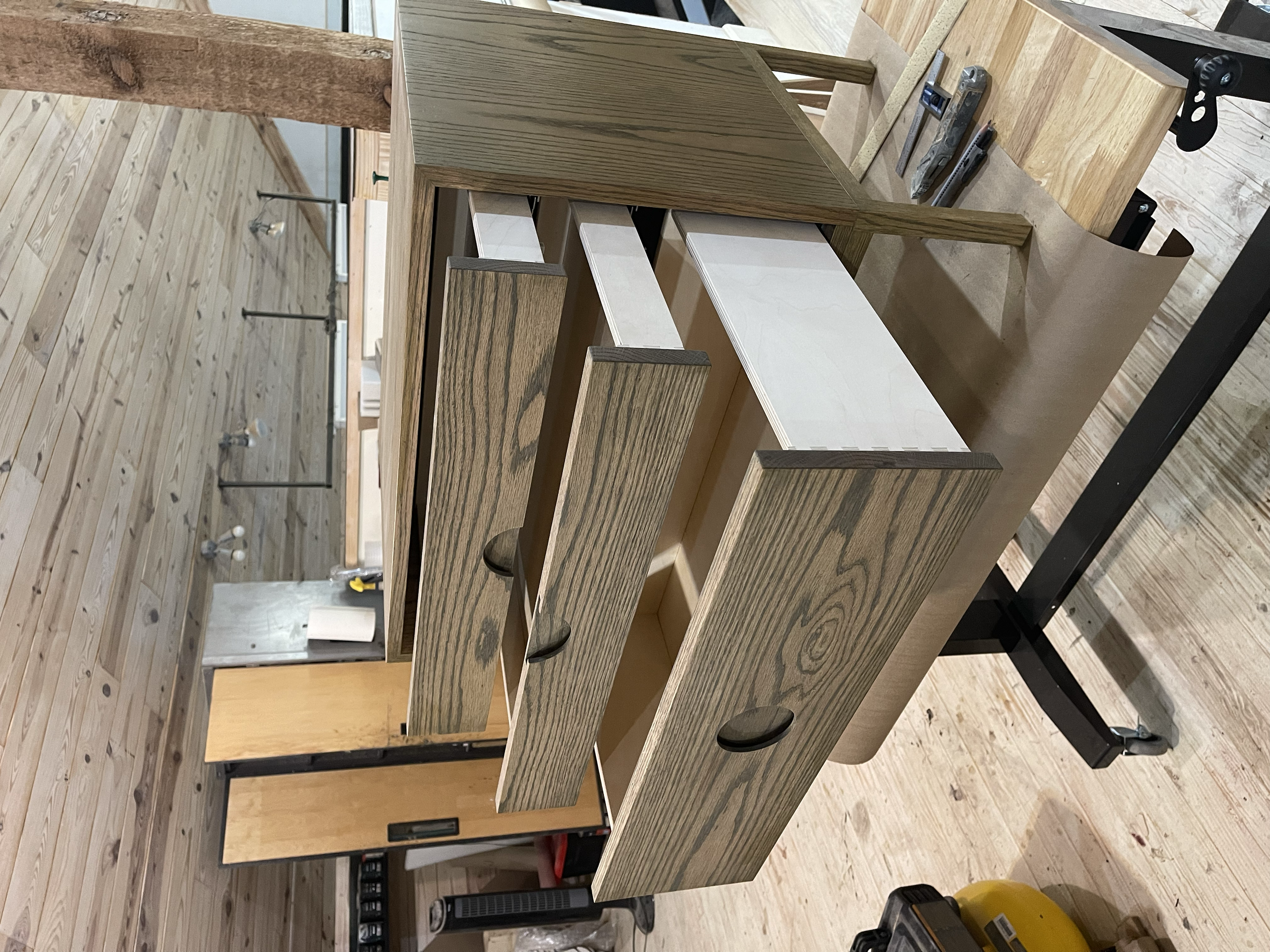 Woodworking workbench with partially assembled wooden drawers and tools in a woodworking shop.