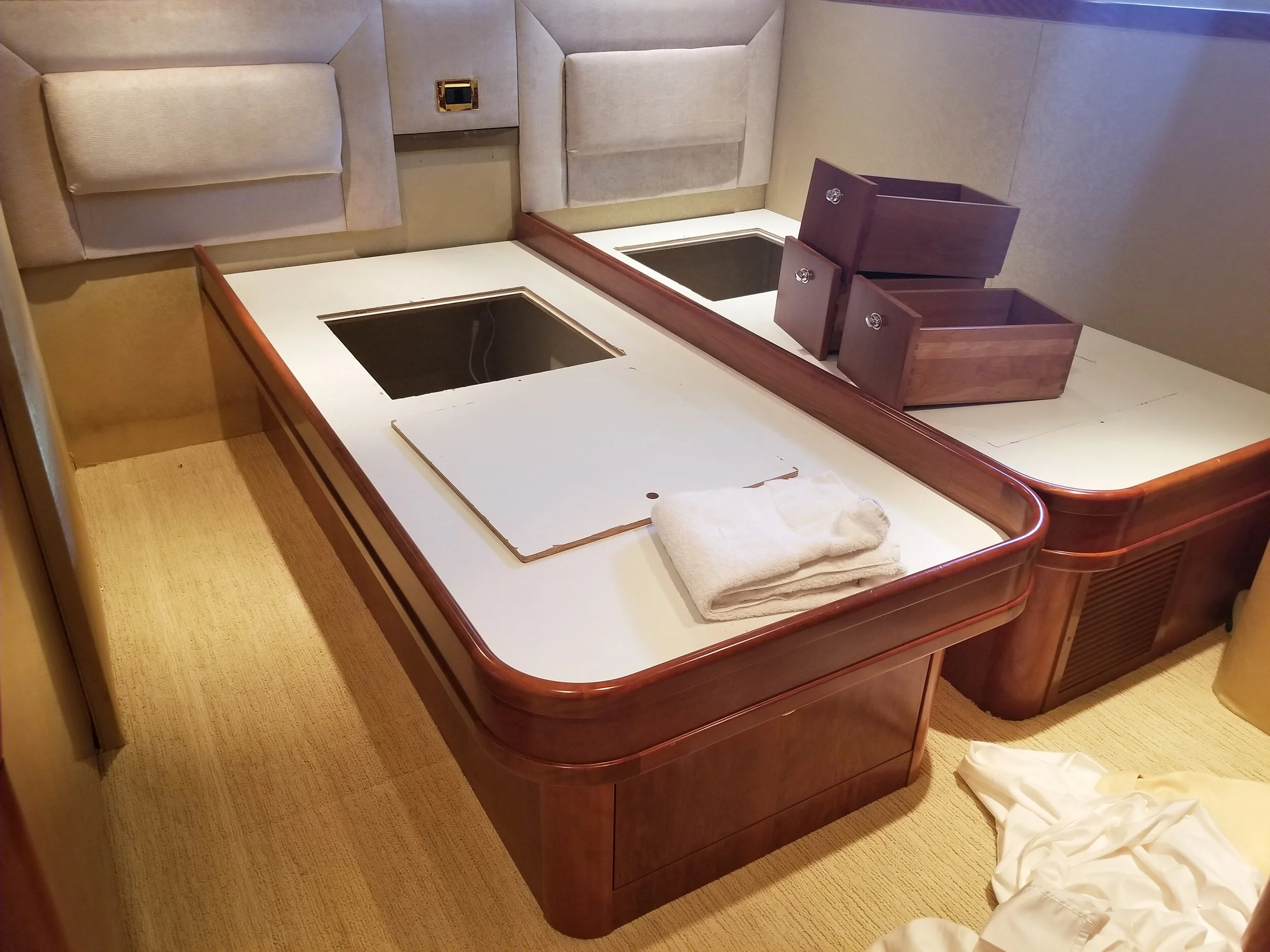 Unmade hotel room table with two built-in glass-covered hot tub sections, folded towels, and two small wooden dresser drawers.