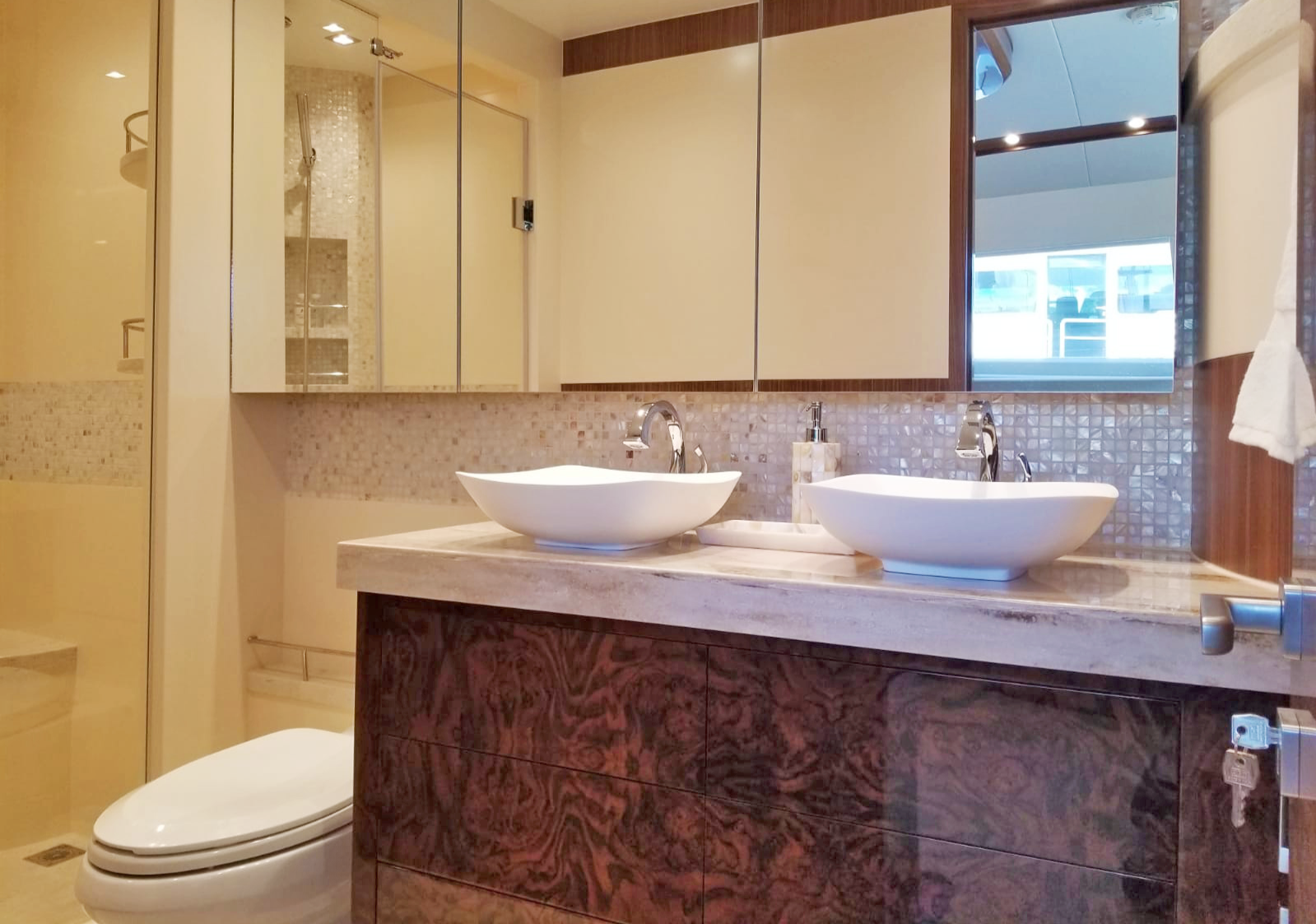 Modern bathroom with dual vessel sinks on a marble countertop, mirrored cabinets, a toilet, and a walk-in shower with glass door.