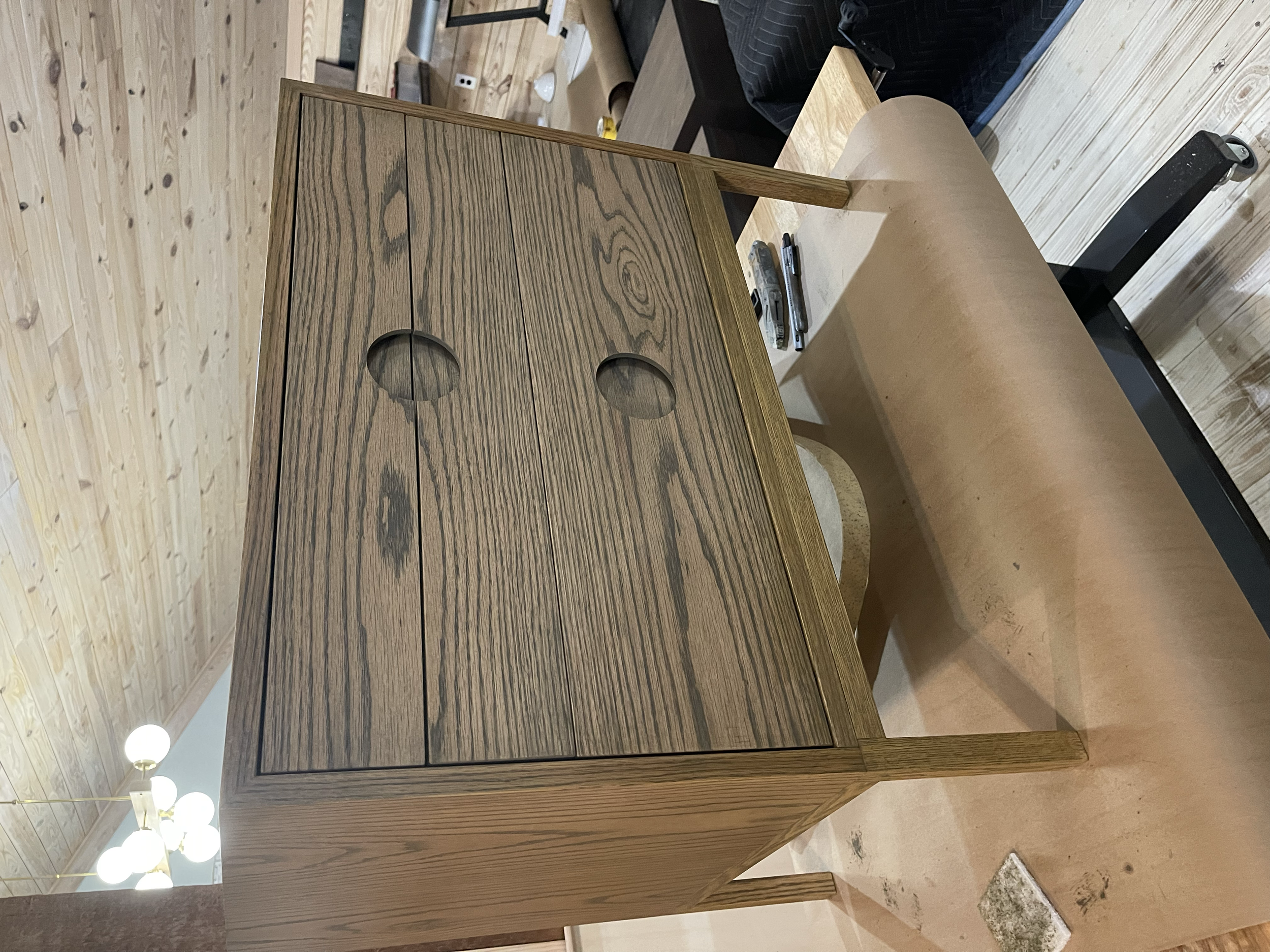 A wooden cabinet with circular cutouts on the doors, placed on a hardwood floor in a room with wood-paneled walls.