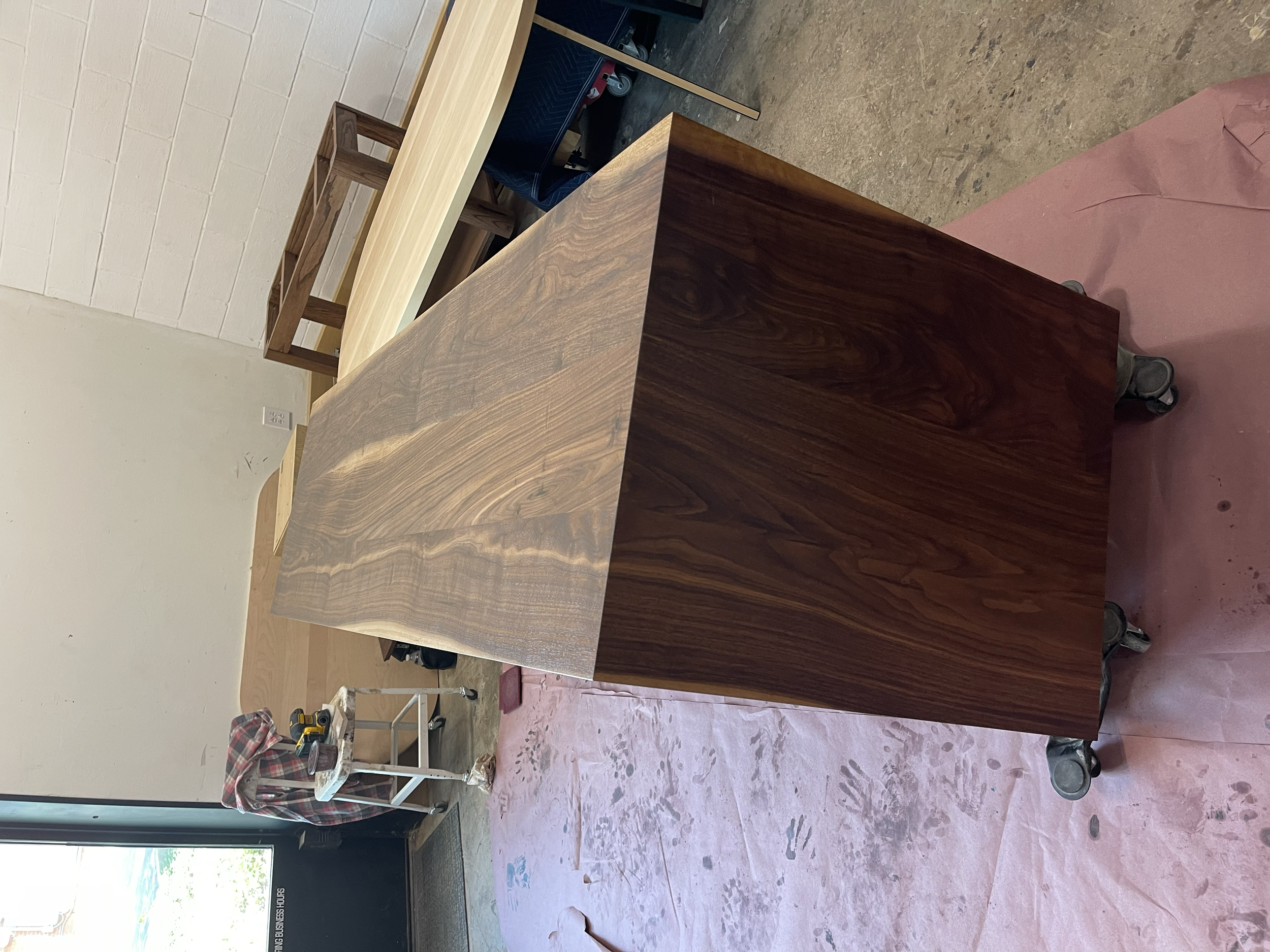 A large wooden piece with a rich, dark wood grain, mounted on wheels, and placed on a pink protective sheet in a workshop.