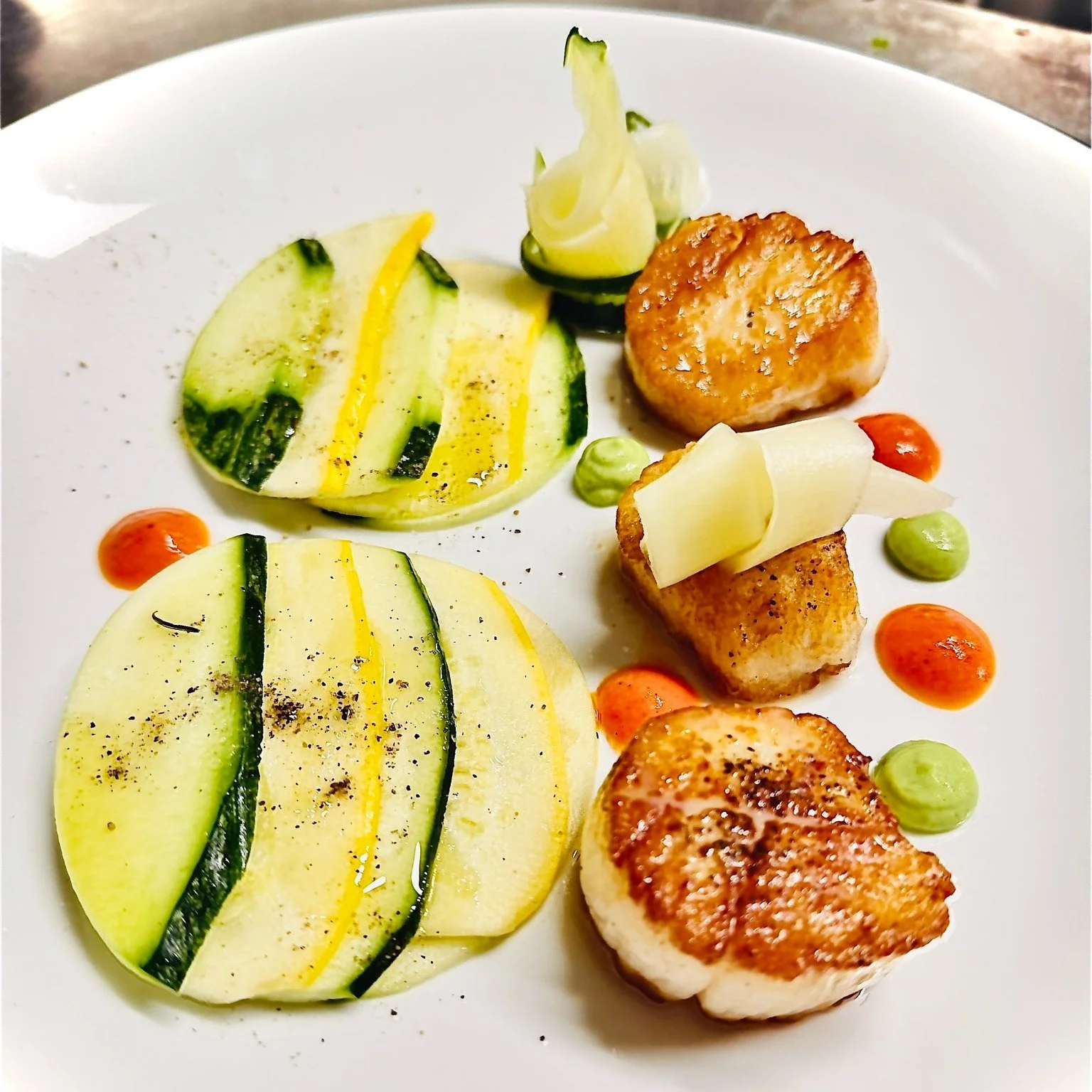 Some dishes whisper instead of shouting.
This week's scallops are one of them.

Perfectly pan-seared sea scallops served with paper-thin rounds of zucchini and summer squash, layered like petals, and finished with a vibrant pea pur&eacute;e and a del