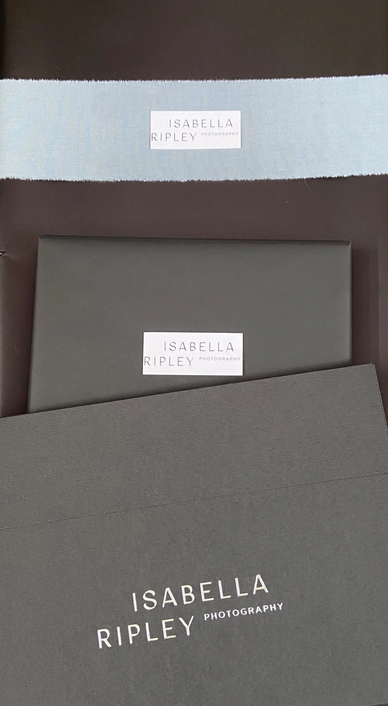 Photographic equipment packaging with boxes and labels featuring the name Isabella Ripley Photography, displayed on a black surface.
