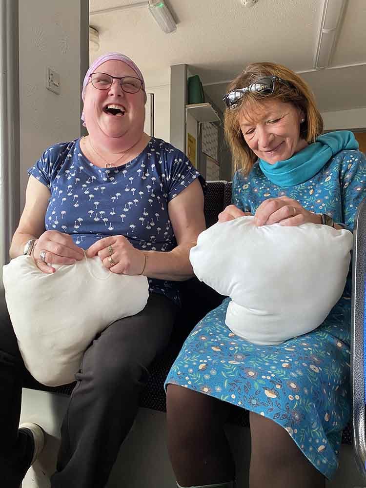 Two perfect hug sewers, laughing and holding white pillows.