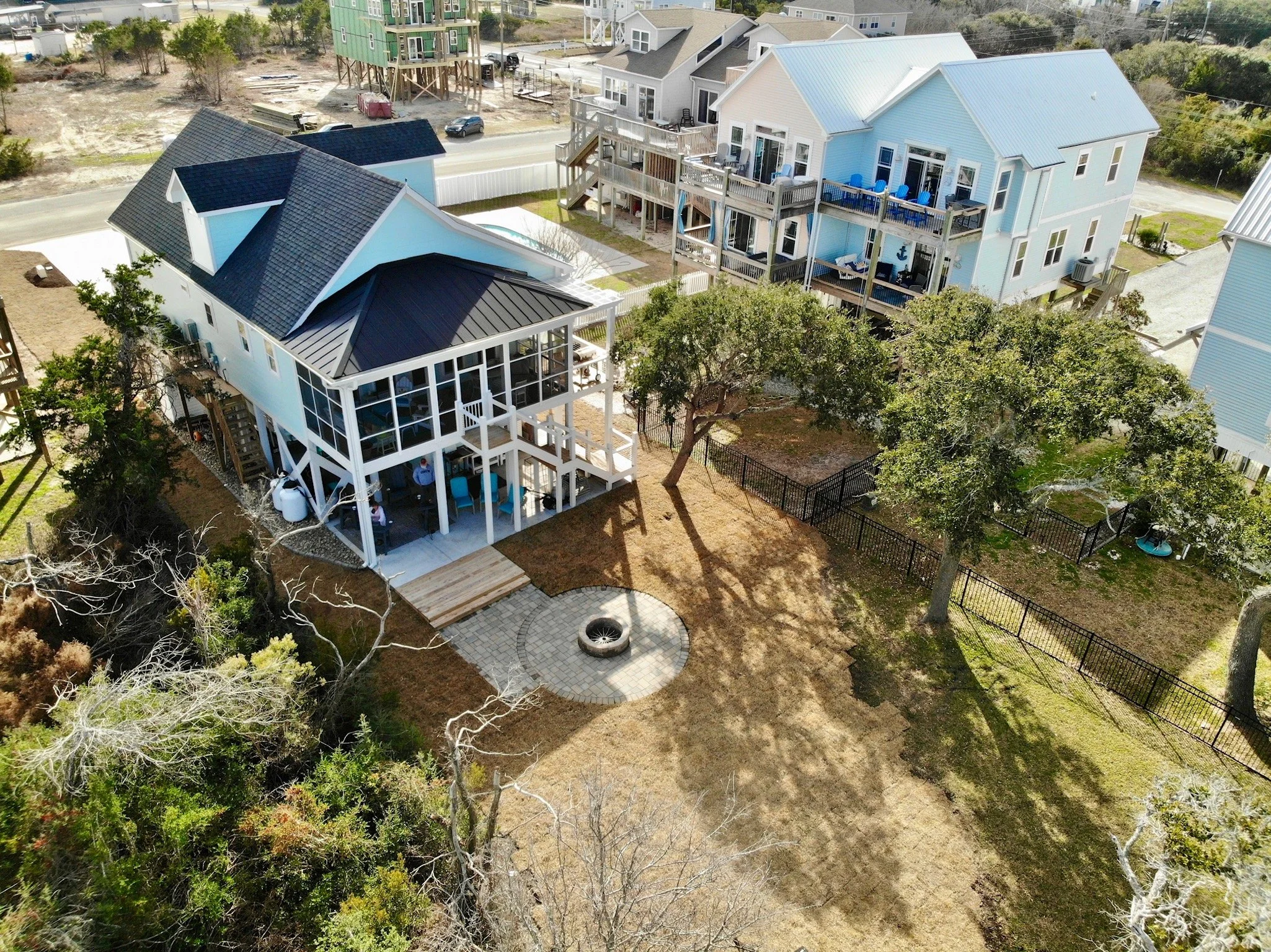 Aerial view of a neighborhood showing several houses with decks, trees, and a construction site in the background.