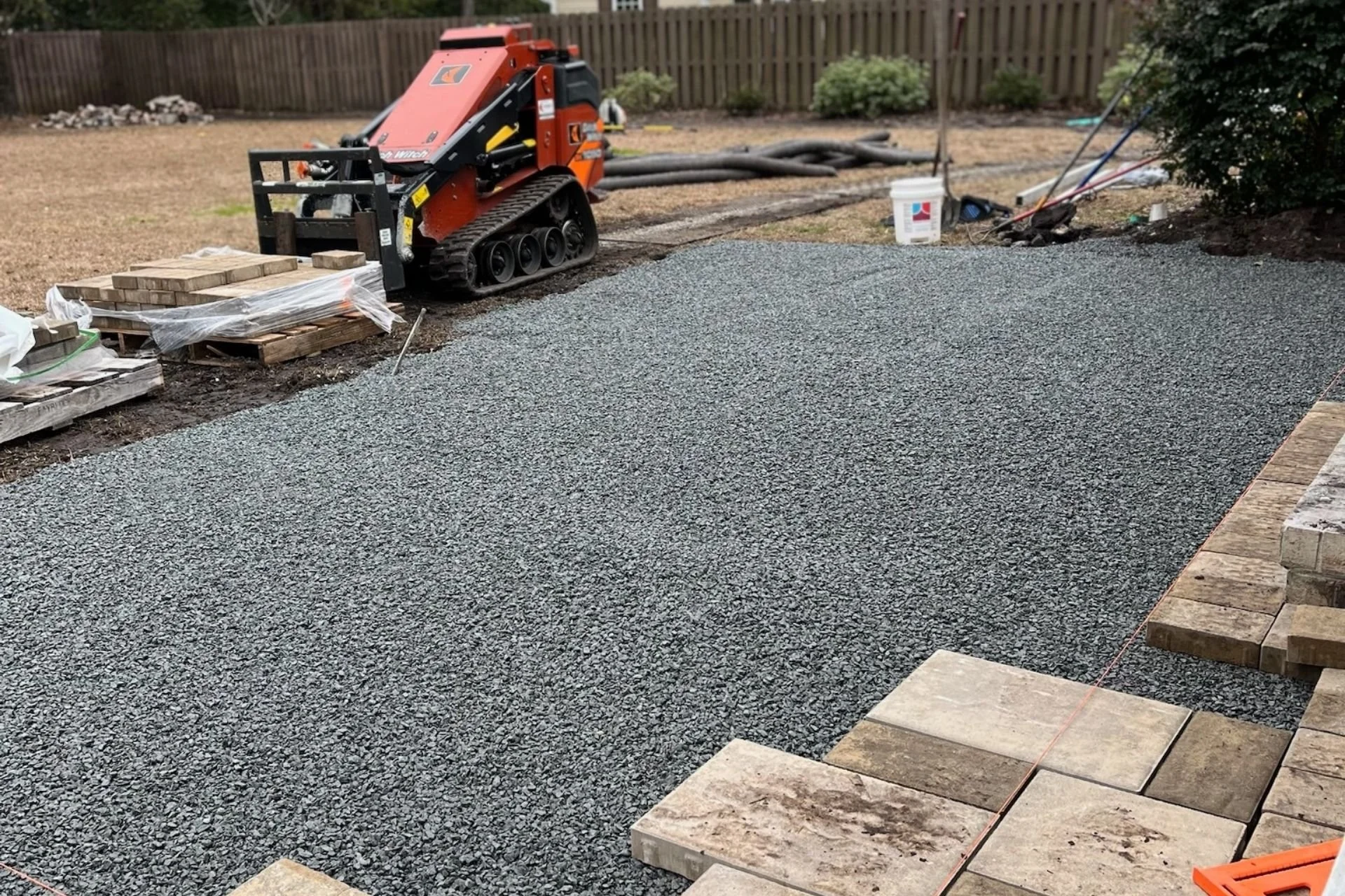 A backyard with smoothed out gravel, paver stones and a small forklift