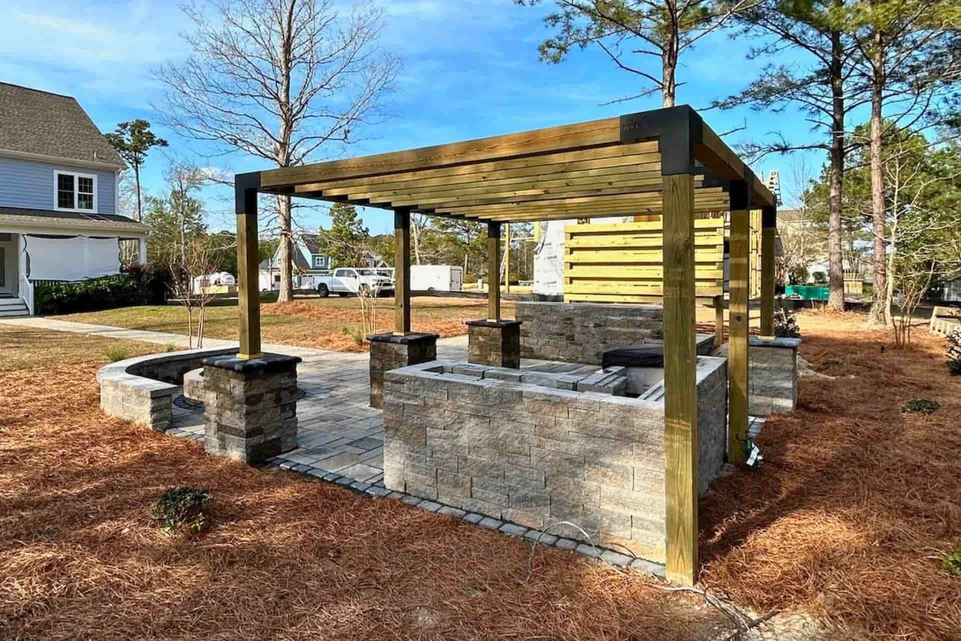 a wooden pergola in a backyard with seating and an outdoor kitchen