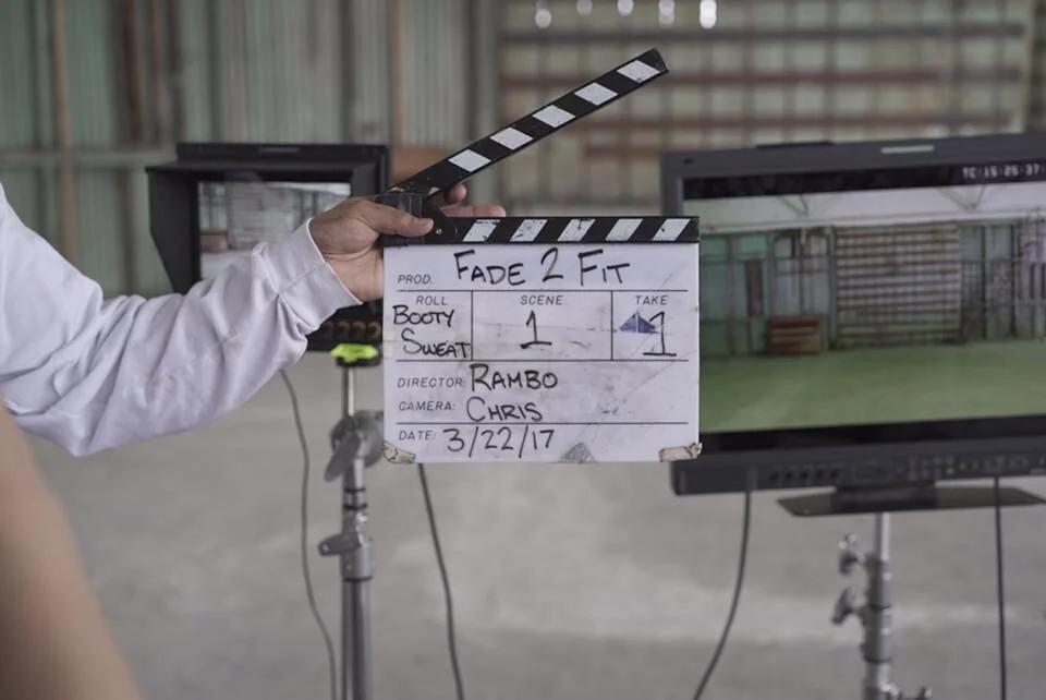 Film slate with 'Fade 2 Fit' written on it, held by a person in a white shirt, in a production setting with a computer monitor in the background.