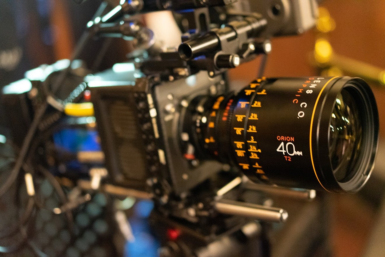 Close-up of a professional camera with a 40mm lens on a film or video set, with blurry background lighting.