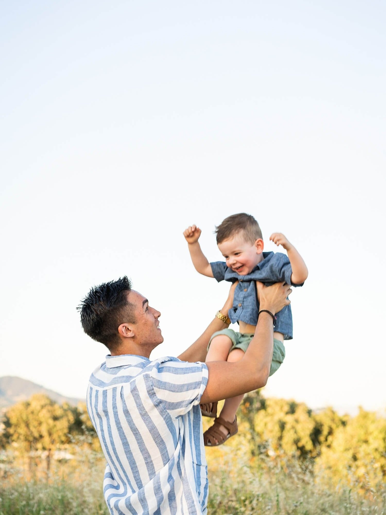 A father lifting his smiling son into the air  – image captured by Sunday Muse Studio