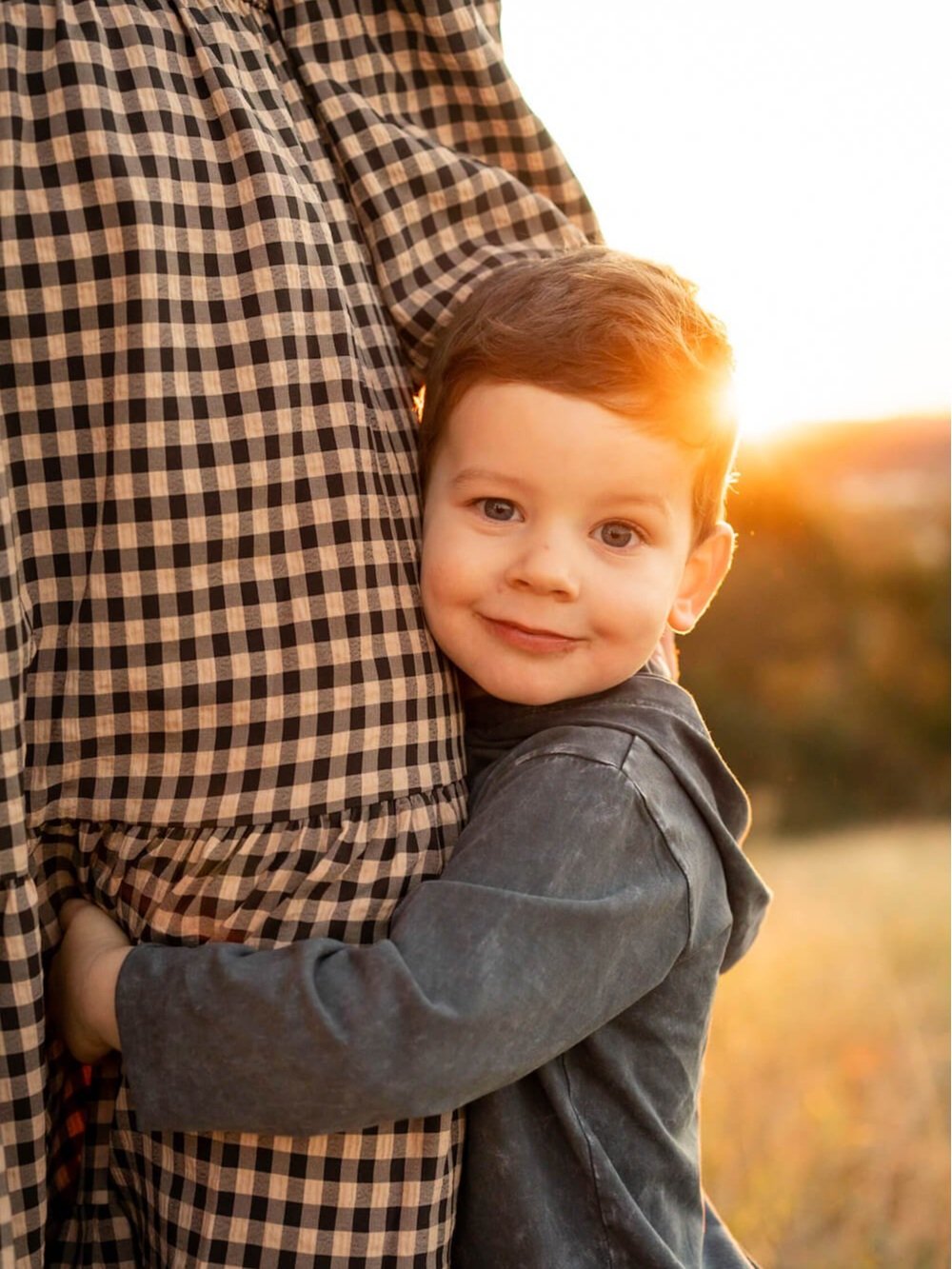 A young boy at golden hour hugging the leg of his mother  – image captured by Sunday Muse Studio