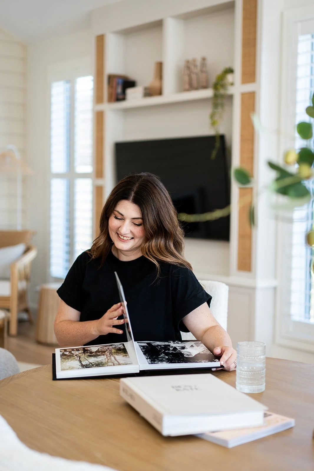 A woman sitting at a light timber table flicking through a photo book.
