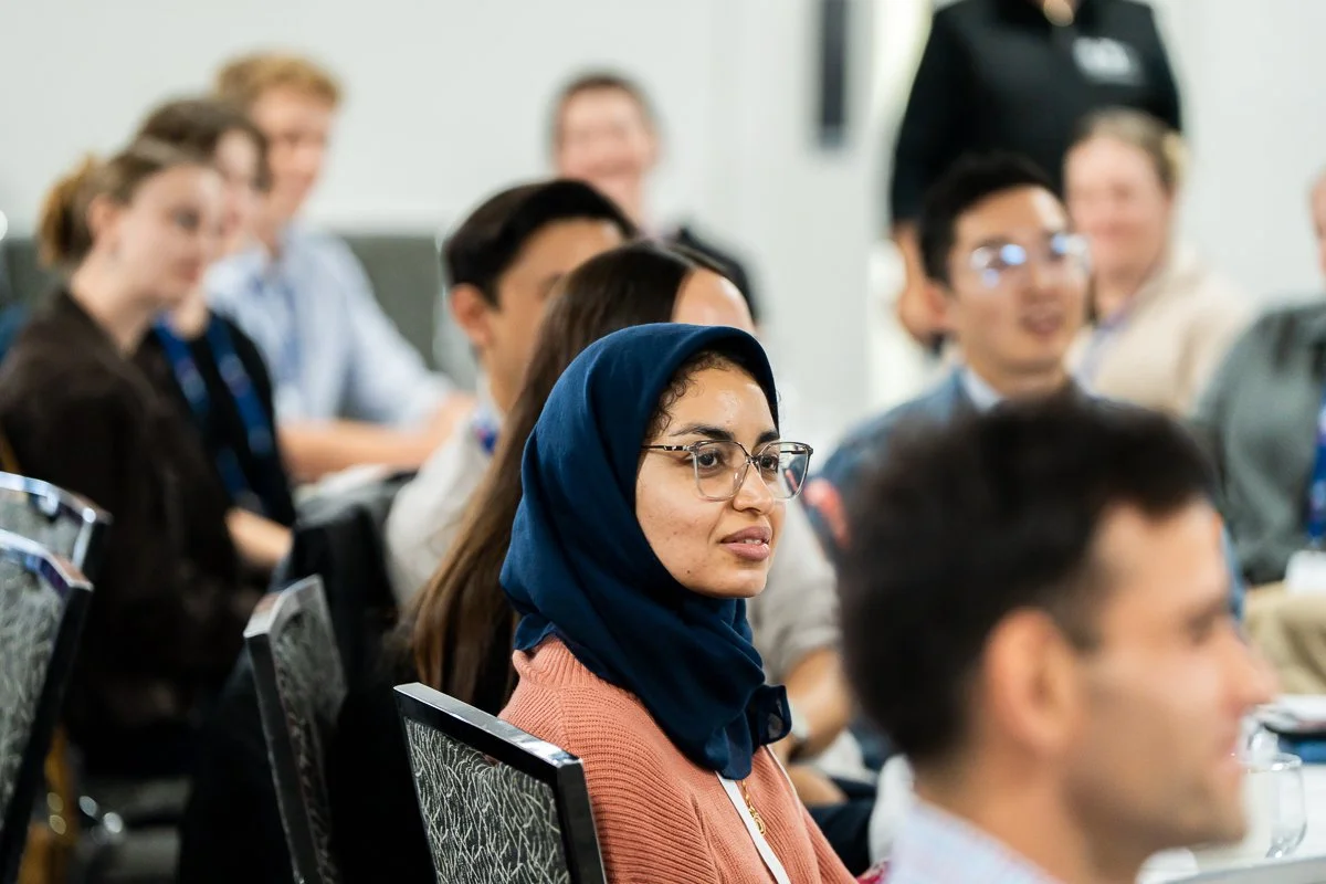 Group of diverse people attending a conference or seminar, sitting in a room with chairs, listening attentively.