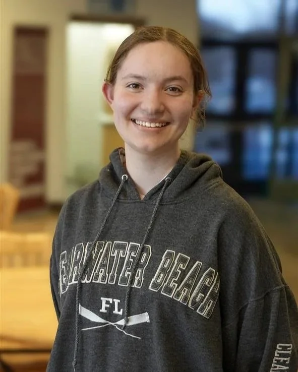 A young woman with red hair smiling indoors, wearing a dark gray hoodie with 'SOUTHWATER BEACH' and 'FL' printed on it.