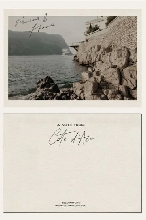 Black and white photo of a rocky coastline with a stone wall, water, and mountains in the background. Handwritten text says "Nice de France." Below, a note reads, "A note from Cote d'Azur," with the website "eluparfums.com".