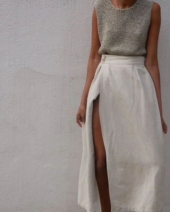 A woman wearing a sleeveless, silver top and a long white skirt with a high slit showing her leg.