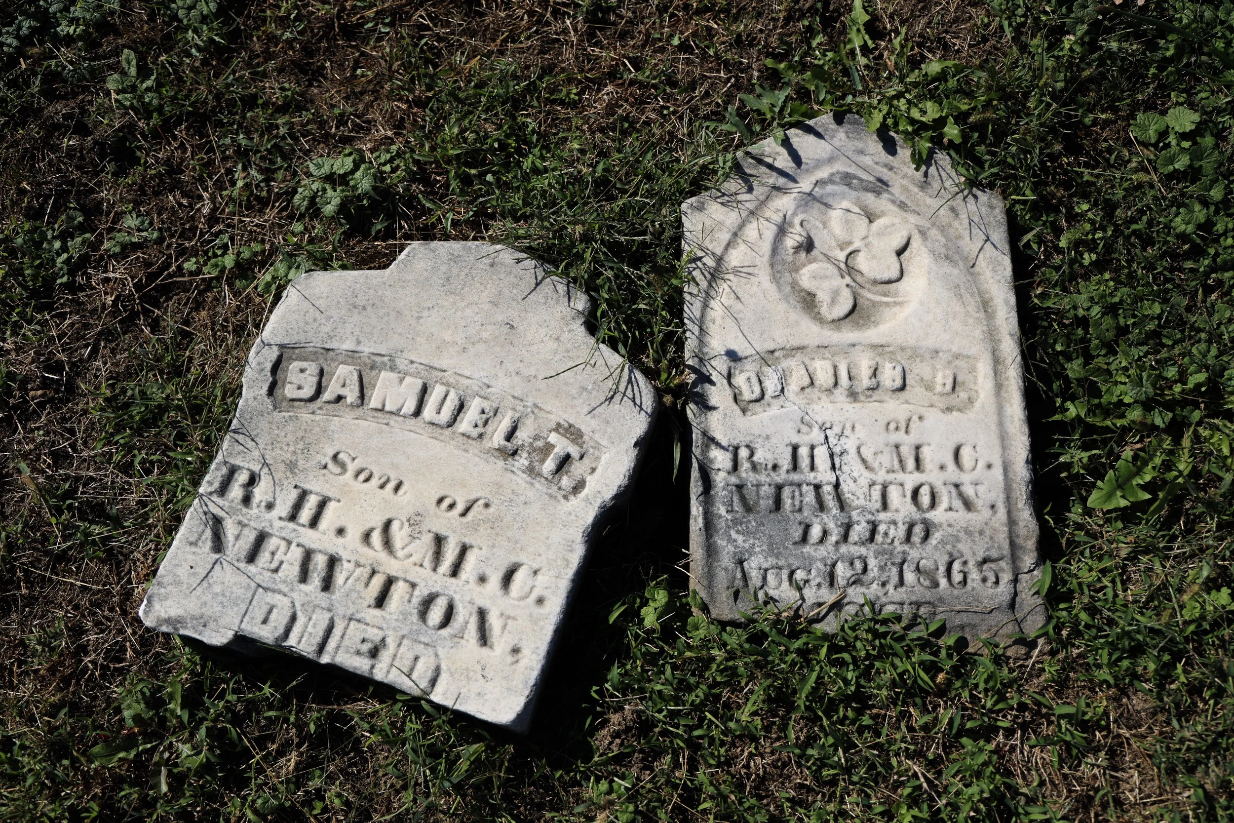 Damaged headstones of two brothers, Samuel and 11-year-old Charles Newton. Because of where Samuel's headstone broke off, his age has been lost. The headstone of their older sister, Eliza, has also been broken and knocked to the ground.