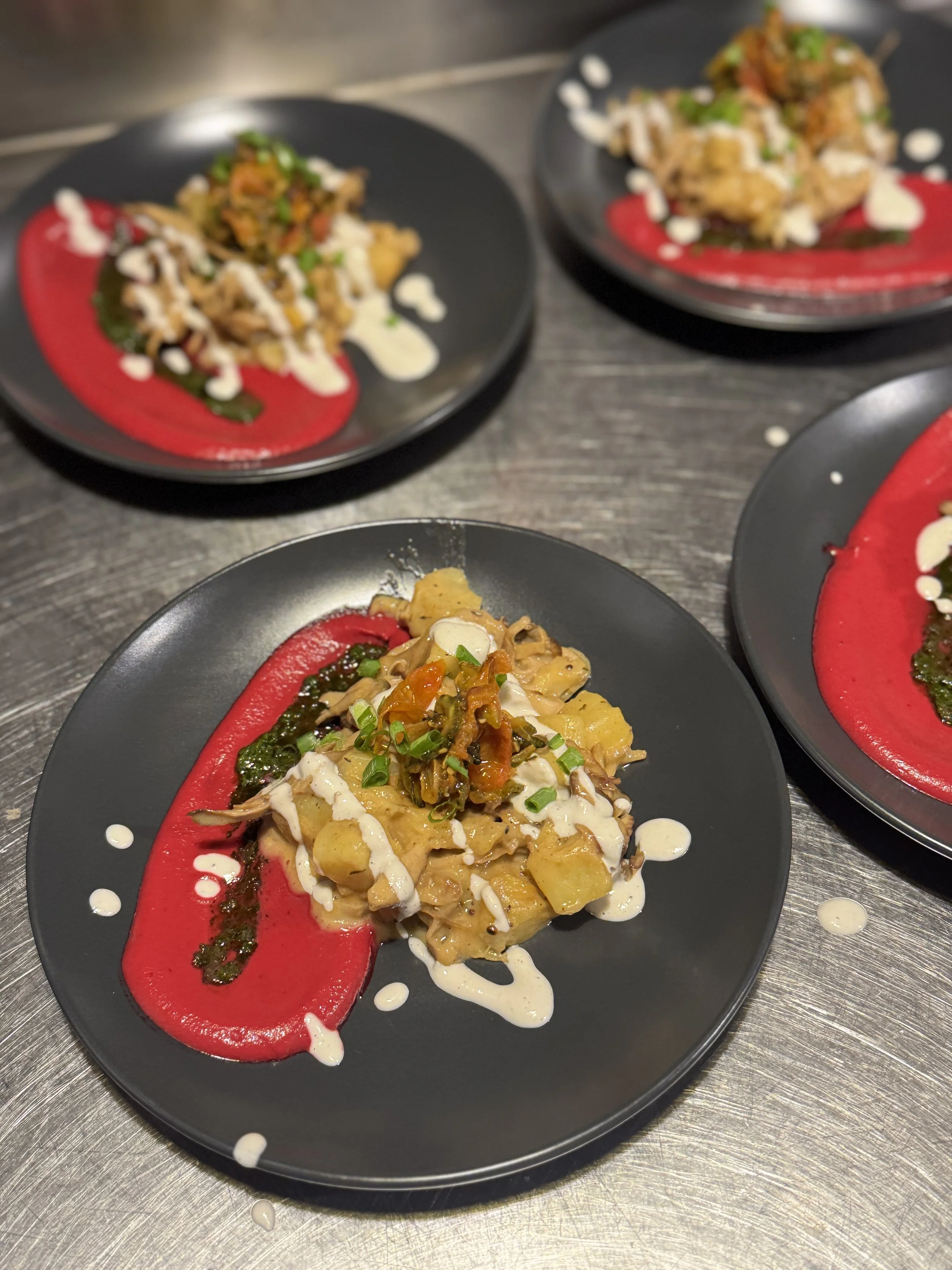 Vegan Fine Dining with Breathwork at Green Peace Inn. In Plates of gourmet food with a red sauce smear, topped with a creamy white sauce and garnished with chopped green onions, served on black plates. 