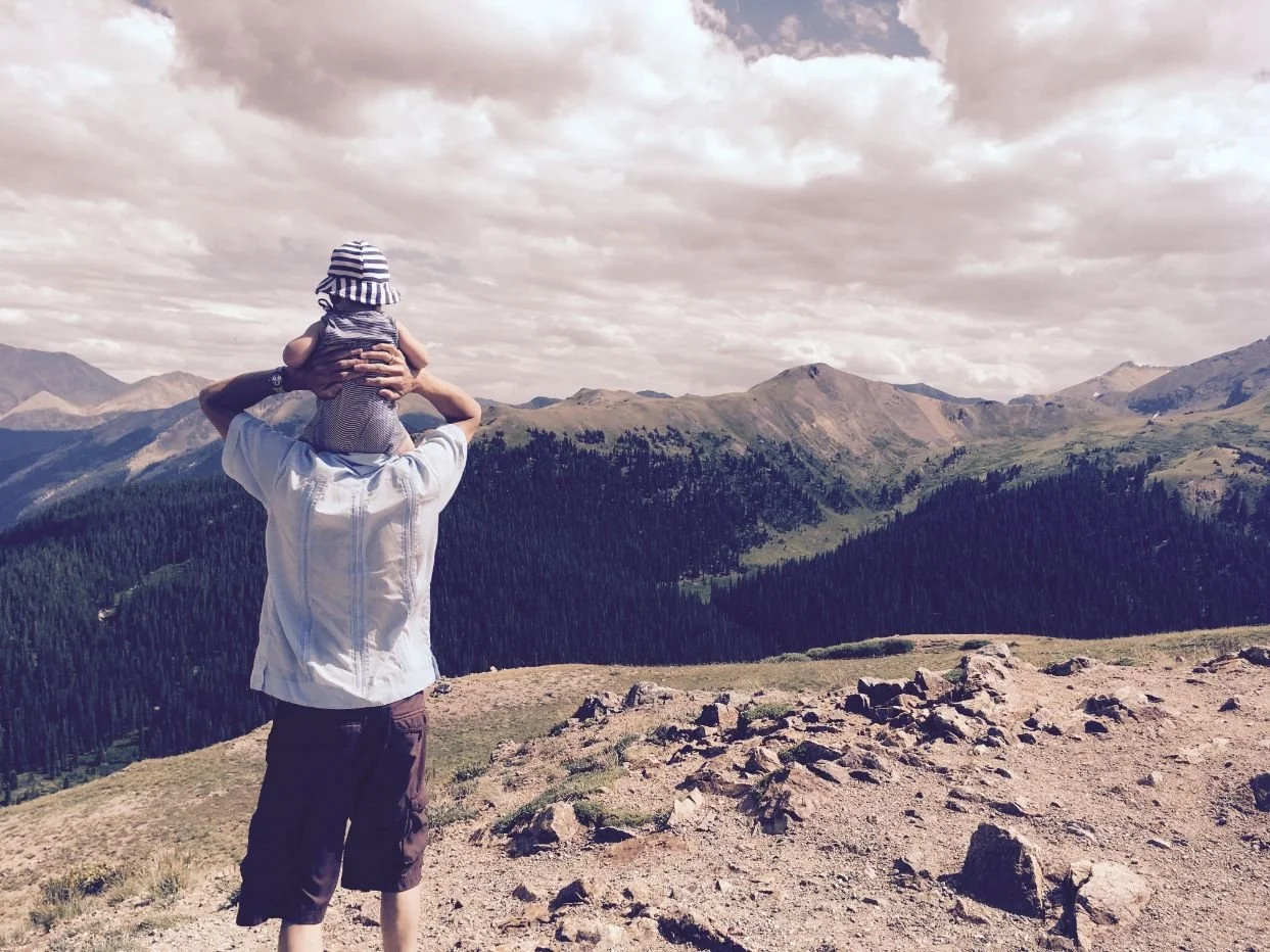 man holding a baby in front of mountains