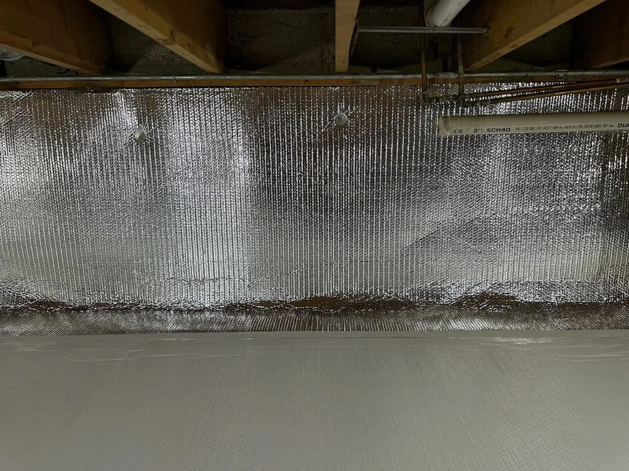 Insulation material installed under a wood floor with pipes running above it.