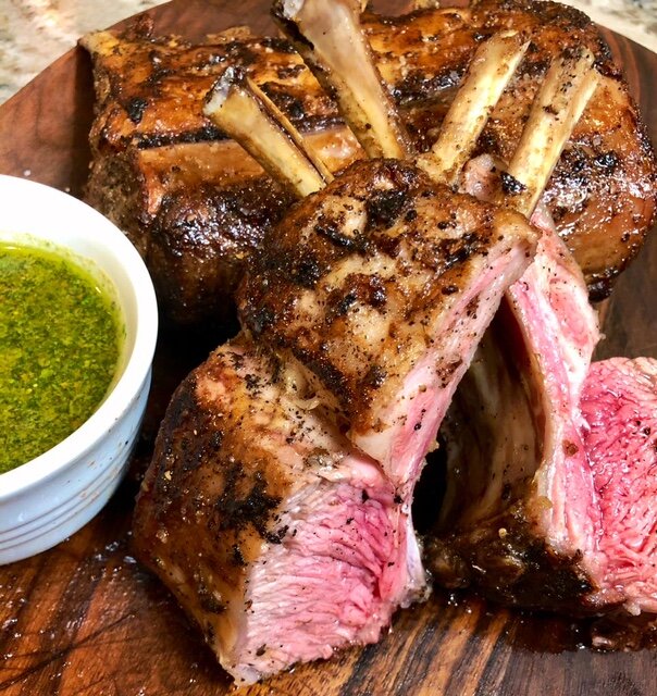 Za'atar Rack of Lamb carved and resetting on a brown cutting board with a sause in a white dish next to it