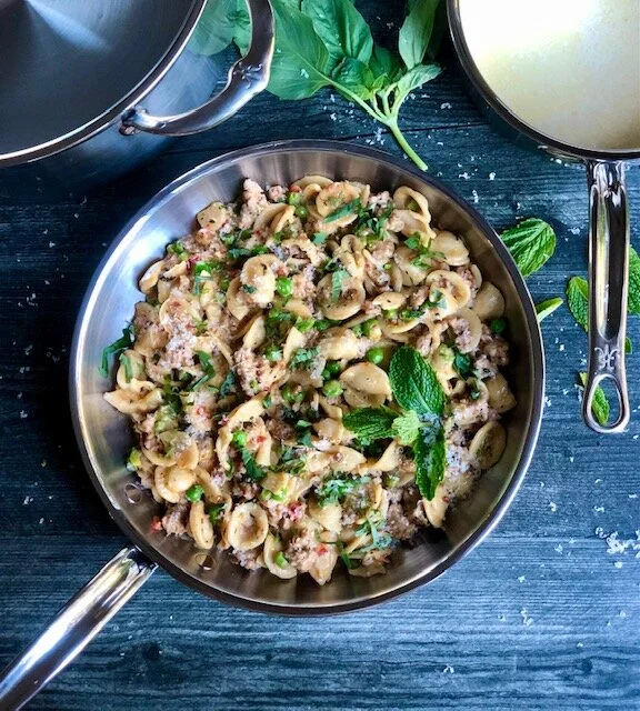 Hestan pan resting on a blue table filled with cooked Sausage Orecchiette Pasta