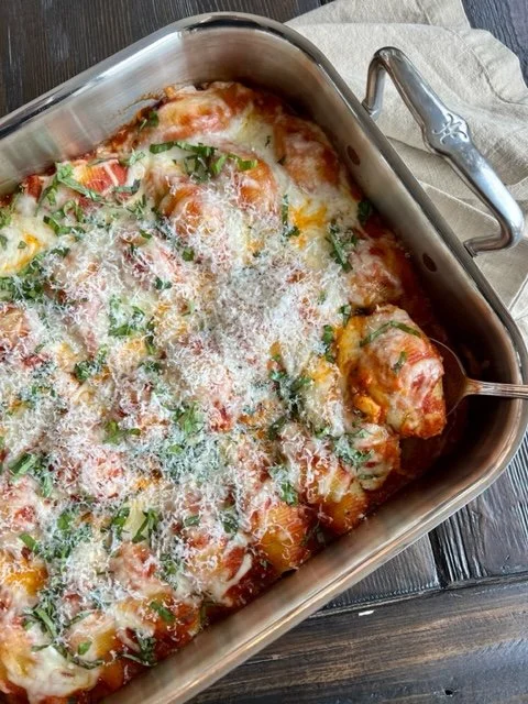 Roasting pan full of Sauage Stuffed Shells placed on a dark wooden table with a linen beige napkin