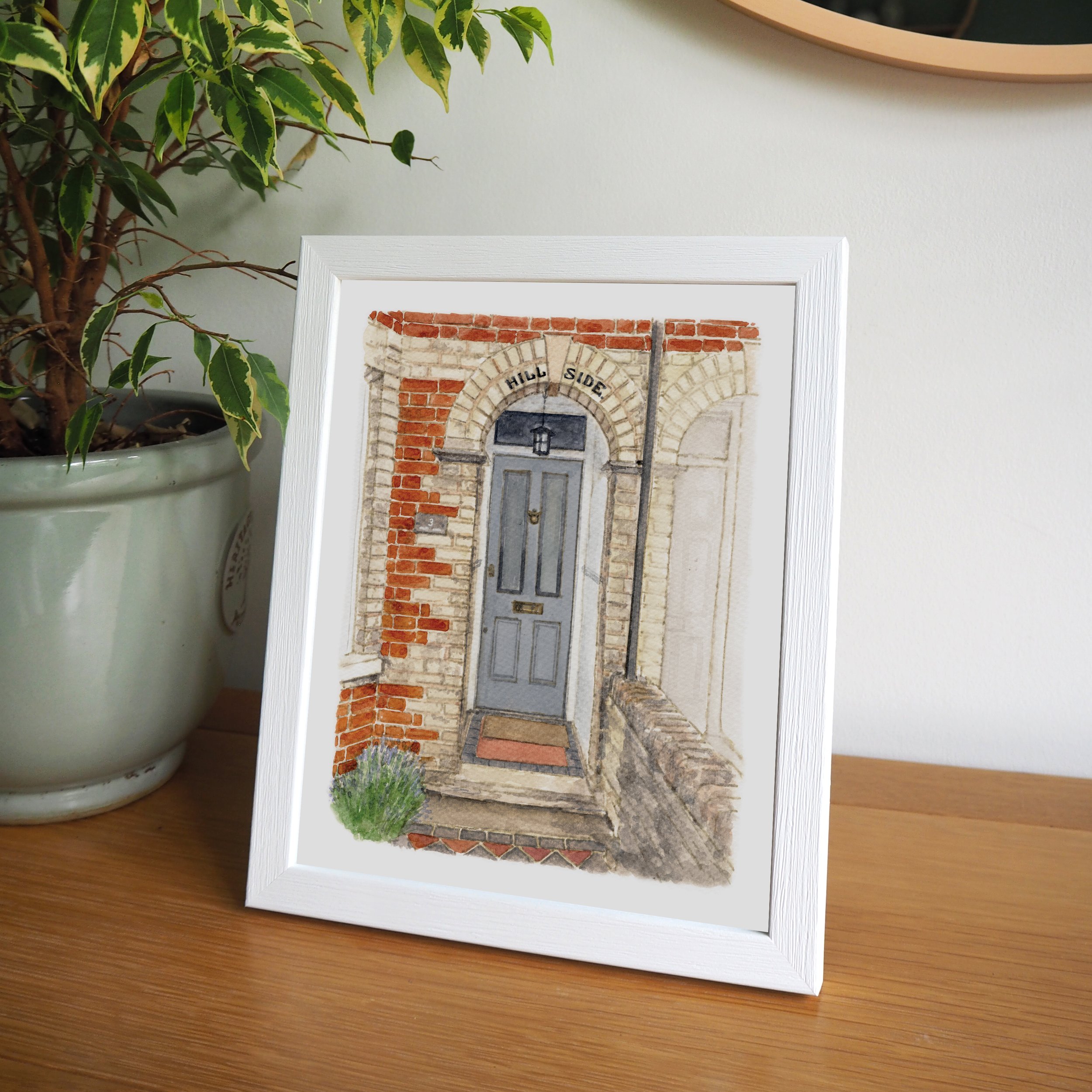 A framed watercolour front door portrait of a grey front door with brick surround and tiled path